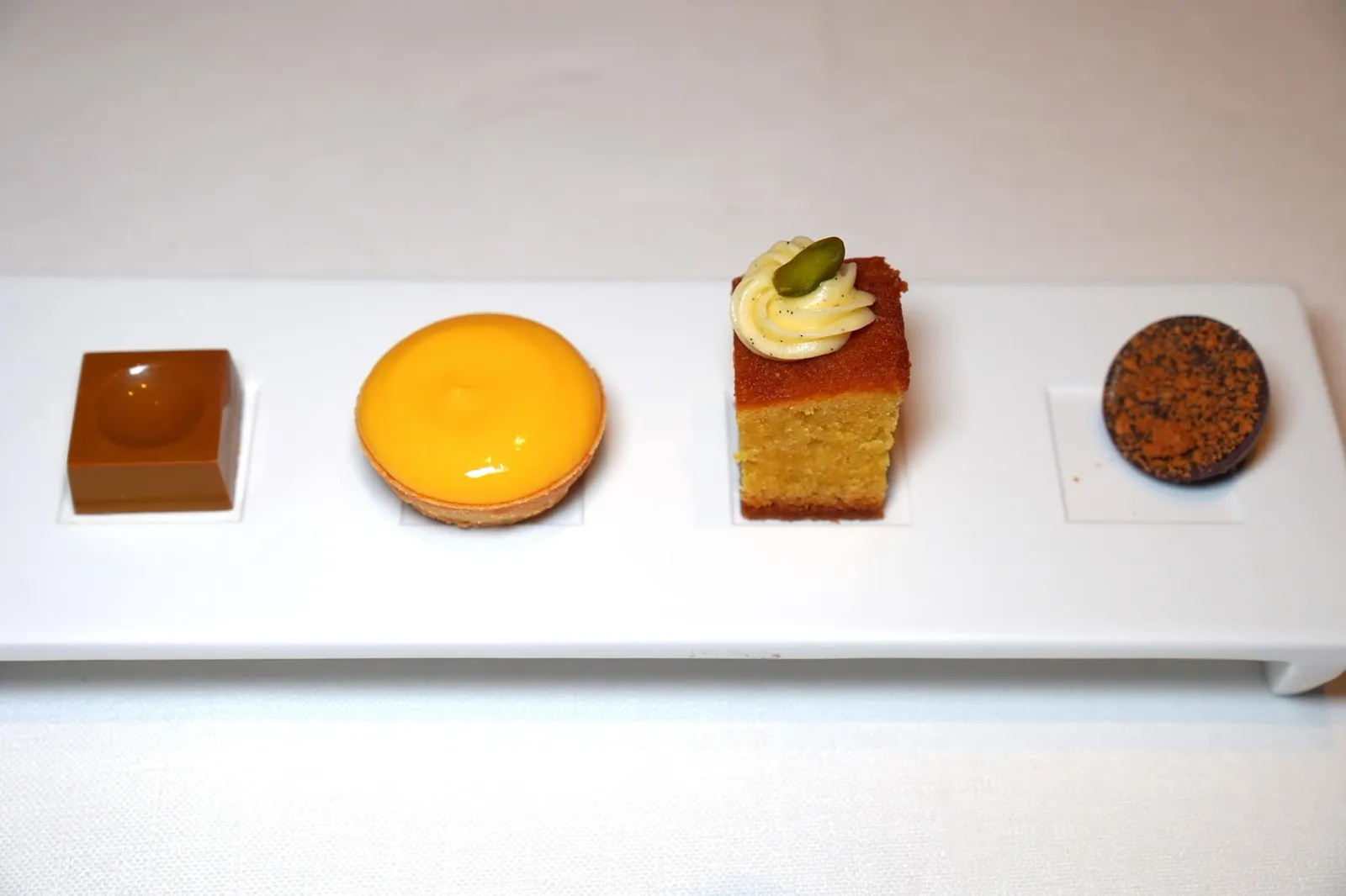 Mignardises สุดท้ายในถาดสีขาวคือ Bonbon with Yuzu, Tartelette with Passionfruit, Pistachio Cake, Bonbon with Cherries and Dutch Cookies