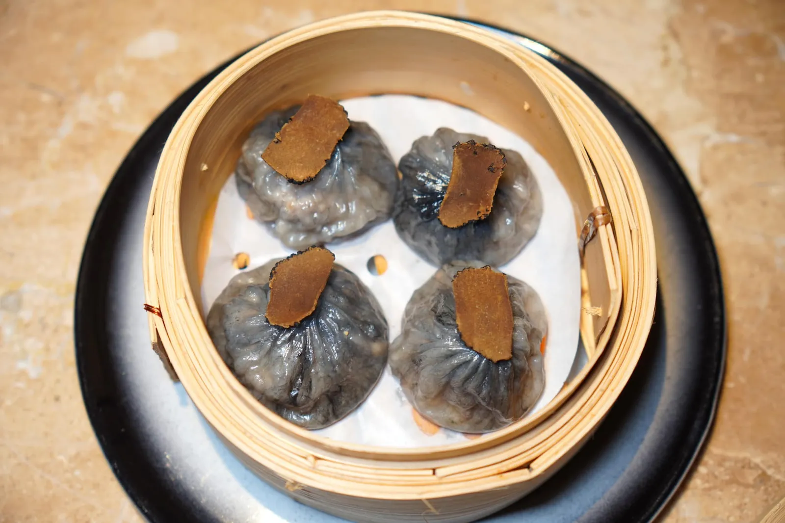 เสี่ยวหลงเปาทรัฟเฟิล (600+) Xiao Long Bao Truffle เสี่ยวหลงเปา ด้านในสอดไส้เนื้อหมูมาพร้อมกับซุปร้อน ๆ และกลิ่นหอมของทรัฟเฟิล ด้านบนท็อปด้วยทรัฟเฟิลสไลด์บางวางแปะมาเพื่อบอกถึงองค์ประกอบสำคัญของจานนี้นั่นเอง