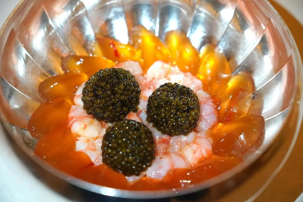 Gamberoni di San Remo, fine galée de poissons de roche, caviar (170 €) Gamberoni from San Remo, rock fish gelée, caviar สำหรับที่สาขาต้นตำรับแห่งนี้เชฟ Alain Ducasse ได้เลือกใช้กุ้งแดงจาก San Remo เมืองเล็ก ๆ ทางตะวันตกเฉียงเหนือของประเทศอิตาลีผสมผสานกับกลิ่นของน้ำมันมะกอกเพียงเล็กน้อย รอบ ๆ เป็นเจลลี่ทำจากปลา Rock Fish มีเนื้อสัมผัสนุ่มละมุนทอปด้านบนด้วยหญ้าฝรั่น จากนั้นเสริมด้วยรสชาติเค็มและอุมามิจากคาเวียร์คุณภาพสูงที่ให้มาจนล้นจาน ถือเป็น Classic of The House ที่ควรค่าแก่การประดับเอาไว้ในสมุดเมนูโดยถาวร นอกจากอาหารรสเลิศในบรรยากาศสุดหรูหราเกินบรรยายแล้วอีกสิ่งหนึ่งที่เป็นที่กล่าวขวัญกันมากในหมู่นักชิมคือราคาของอาหารแต่ละจานโดย Gamberoni จานนี้ถูกตั้งราคาเอาไว้ที่ 170 € หรือประมาณ 6,600 บาทเลยทีเดียว (20/20)