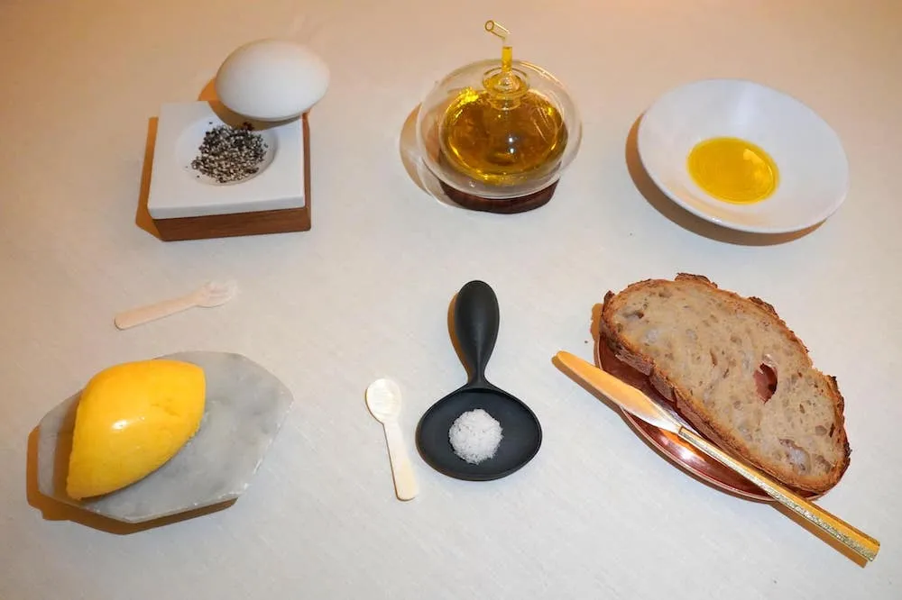 Truffle Wheat Bread สำหรับขนมปังอย่างแรกคือ Truffle Wheat Bread เสิร์ฟมากับองค์ประกอบอื่น ๆ คือ Brittany Salted Butter ซึ่งเป็นเนยที่ได้มาจากแถบตะวันตกเฉียงเหนือของประเทศฝรั่งเศสทำมาเป็น Quenelle เสิร์ฟมาบนหินอ่อนซึ่งมีความเย็นมากกว่าอุณหภูมิห้องป้องกันไม่ให้เนยละลายได้โดยง่าย ตัวเนยให้กลิ่นหอม รสชาติมันและเค็มพอเหมาะ ยังมี Sarawak Black Pepper หรือพริกไทยดำคุณภาพสูงจากแถบซาราวักในประเทศมาเลเซีย ตรงกลางคือเกลือจาก Guérand ซึ่งเป็นแหล่งผลิตเกลือชั้นเยี่ยมทางตะวันตกเฉียงเหนือของประเทศฝรั่งเศสเช่นกันเสิร์ฟมาพร้อมช้อนทำมาจากเปลือกหอย สุดท้ายคือน้ำมันมะกอกท้องถิ่นจากแถบเมือง Nice ซึ่งขึ้นชื่อว่าเป็นแหล่งผลิตน้ำมันมะกอกที่ที่สุดอันดับต้น ๆ ของโลกอีกด้วย