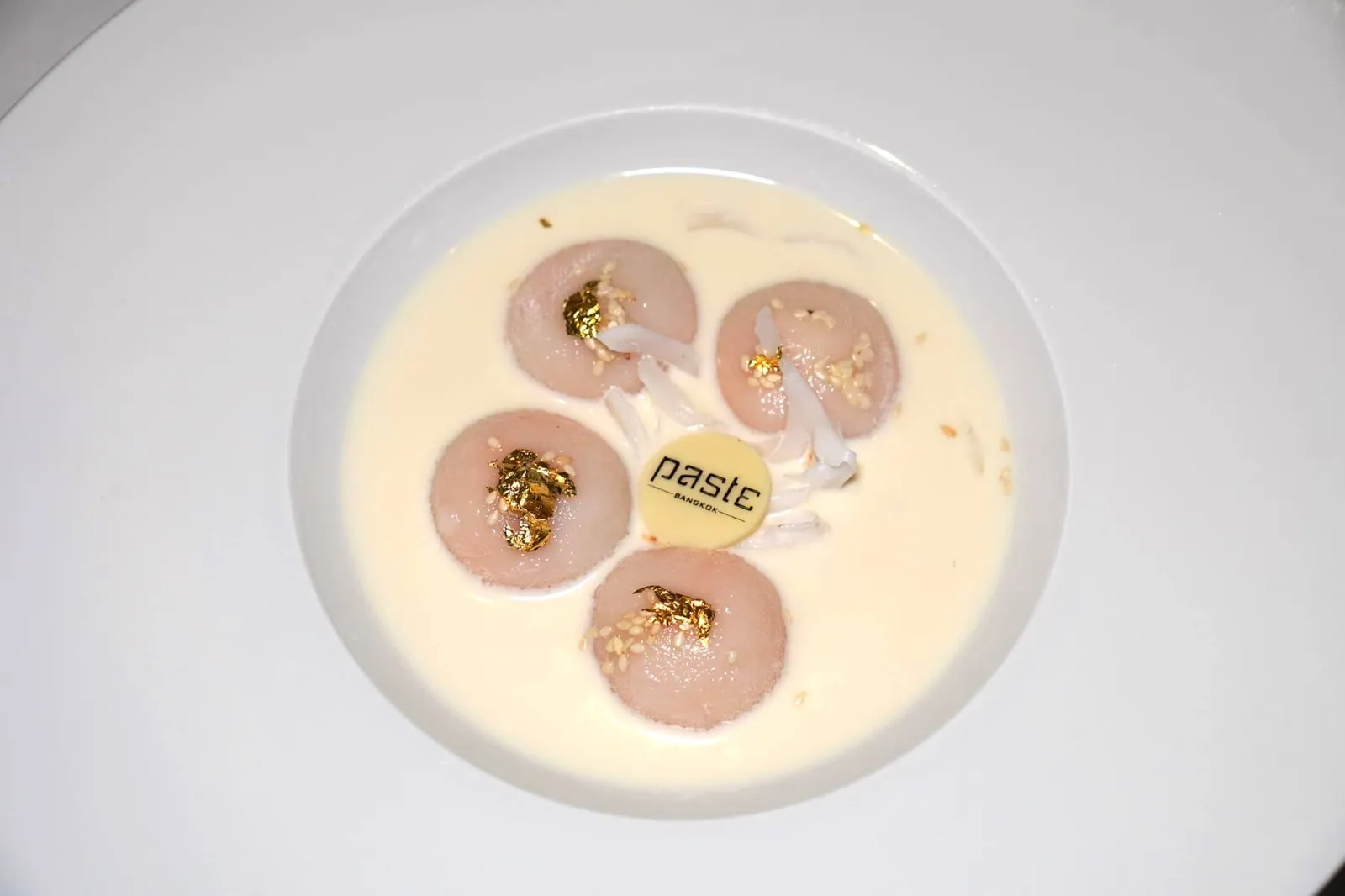 บัวลอยไข่เค็มลาวา (550++) Floating on the Fresh milk infused with longan honey บัวลอยไข่เค็มลาวาจานนี้เชฟนำแป้งมาสอดไส้ด้วยไข่เค็มลาวาที่จะละลายในปากเทื่อเคี้ยว ด้านบนโรยด้วยงาขาว จากนั้นประดับด้วยทองคำเปลวรับประทานได้ เสิร์ฟมาคู่กับมะพร้าวอ่อน และซอสนมสดหอมมัน (15/20)