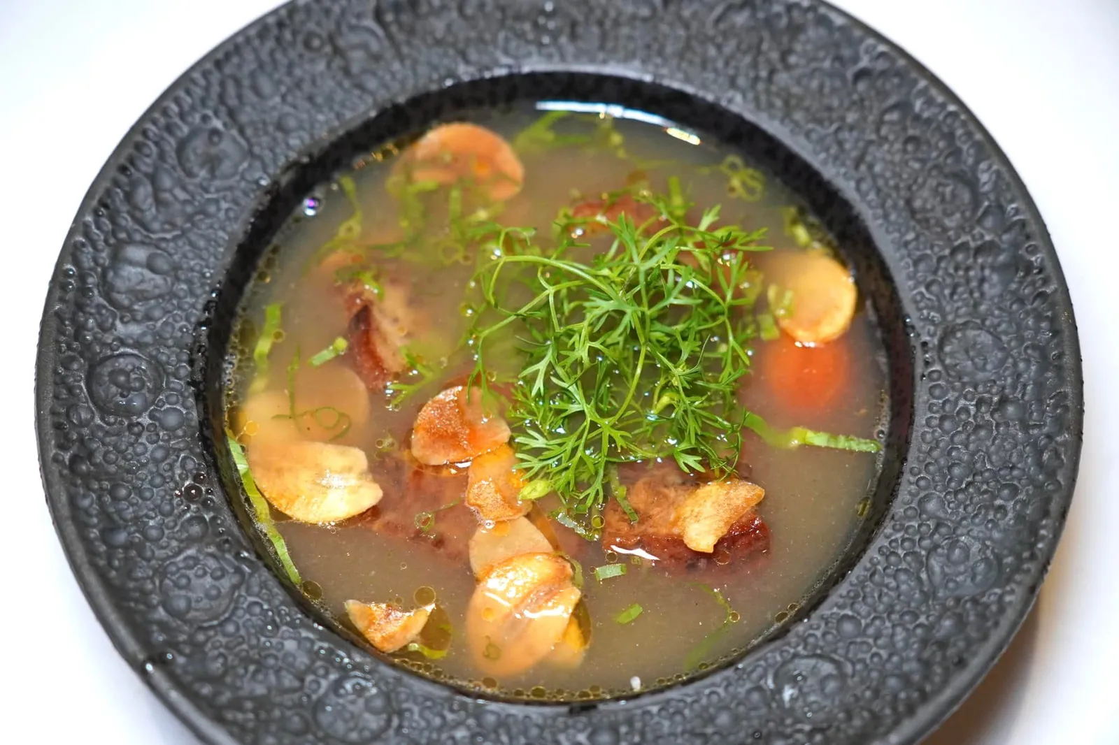 ต้มยำเม็ดขนุนและขาหมูโบราณใส่หอมแดงเผา (650++) Old style hot & sour soup of crisp pork leg, jackfruit seeds & smoky chicken broth ต้มยำขาหมูเสิร์ฟมาแบบน้ำใสตามตำรับโบราณโดยใช้น้ำสต๊อกไก่ทำให้ตัวซุปค่อนข้างเบา (Light) เพื่อที่จะสามารถชูองค์ประกอบอื่น ๆ ให้โดดเด่นขึ้นมาได้โดยง่าย ส่วนรสชาตินั้นมีระดับความเผ็ดจีดจ้านพอประมาณ มีรสเปรี้ยวอุมิมาจากมะเขือเทศ นอกจากนี้ยังมีองค์ประกอบของมะเขือเผาและหอมแดงเผาทำให้ตัวน้ำซุปเองมี Smoky Aroma แทรกอยู่มากจนหอมขึ้นจมูก ขาหมูมีความมันและความกรอบนิด ๆ แต่ไม่เหนียวติดฟัน ยังมีเม็ดขนุนใส่ลงไปเพื่อเพิ่มเนื้อสัมผัสที่ดีอีกด้วย (15/20)