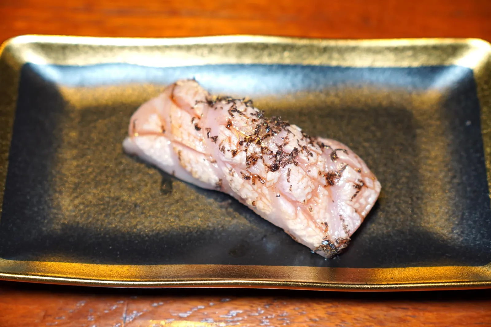 Ootoro Nigiri Sushi โอโทโร่หรือส่วนท้องของปลาแซลมอนที่มีอัตราส่วนไขมันสูง เชฟนำมาทอร์ชเล็กน้อยให้มีไขมันบางส่วนละลาย กัดแล้วสัมผัสได้ถึงความนุ่มและความมันที่พอดีเต็มปากเต็มคำ ด้านบนทอปด้วยทรัฟเฟิลขูดเข้ากันดีกับกลิ่นหอมของมันปลา