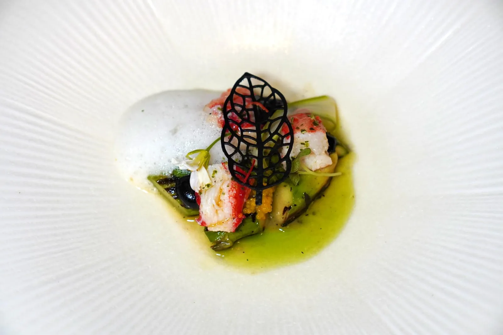 Tom Yum / King Crab / Galanga ห้ามพลาดเมนู Signature Dish ประจำร้านอย่างต้มยำปูคิงแครบ เชฟนำปูคิงแครบไปปรุงสุกเพียงเล็กน้อยในเนยกุ้งล็อบสเตอร์ ข้าง ๆ กันคือหน่อไม้ฝรั่งย่างบาบีคิวสไตล์ญี่ปุ่น ยังมีองค์ประกอบของครีมกระเทียมดำและแผ่น Tuile กรอบทำมาจากกระเทียมดำเช่นกัน น้ำมันสีเขียวทำมาจากใบมะกรูด สุดท้ายคือ Coconut Milk Emulsion หรืออีมัลชั่นน้ำกะทิที่มีเครื่องเทศผสมอยู่ด้วย (15/20)