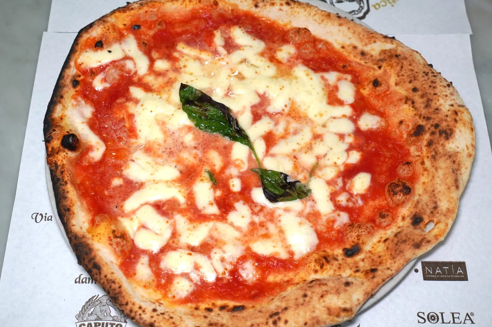 MARGHERITA (5 €) pomodoro, fior di latte, olio, basilico สูตรแป้งพิซซ่านี่จะได้รับการเตรียมขึ้นมาบริเวณชั้นสองของร้านโดยมีองค์ประกอบทั้งหมดเพียง 4 อย่างคือแป้ง 00 แบรนด์ Caputo Blu ถุงสีน้ำเงิน, ยีสต์, เกลือ และน้ำผสมเข้าด้วยกันในเครื่องนวดแป้งนาน 40 นาทีจนถึงจุดที่เรียกกันว่า Punto di Pasta สังเกตได้จากการที่ตัวแป้งมีความเงาสะท้อนแสงและหนึบสู้มือ จากนั้นจึงพักเอาไว้นาน 24 ชั่วโมง หลังจากพักแป้งมาได้ 1 วันทีมเชฟจะนำแป้งมาตัดด้วยมือโดยใช้อุปกรณ์โลหะคล้ายมีดขนาดเล็กให้แต่ละชิ้นมีน้ำหนักประมาณ 300-320 กรัมก่อนจะใช้นิ้วโป้งนวดให้กลายเป็นก้อนกลมแล้วนำไปพักในถาดไม้ต่ออีก 4-5 ชั่วโมง จากนั้นเชฟจะแป้งลงมาบริเวณชั้นล่างเพื่อเตรียมเสิร์ฟโดยการคลึงพิซซ่าด้วยเทคนิคเฉพาะตัว ในส่วนของพิซซ่าสุดคลาสสิคของทางร้านอย่าง Margherita นั้นเชฟจะใช้ Pomodoro di Campania หรือมะเขือเทศจากแคว้น Campania ทาลงไปทั่วแผ่น จากนั้นใส่ Fior di Latte di Agerola ซึ่งเป็นชีสมอซซาเรลลาชนิดหนึ่งรวมไปถึง Seed Oil หรือน้ำมันเมล็ดธัญพืชจบด้วยการโรยชีส Pecorino Romano ลงไปทั่ว ๆ หลังจากเตรียมหน้าพิซซ่าได้ที่เชฟจะคลึงลงบนไม้พายเพื่อให้ชิ้นพิซซ่ามีขนาด หญ่ตามคอนเซป A Ruota di Carro หรือ Wagon Wheels อย่างที่กล่าวไปข้างต้นและนำเข้าไปอบใน Stefano Ferrara Forni หรือเตาฟืน Classic Neapolitan ที่นิยมใช้ดันในร้านพิซซ่าชั้นสูงทั่วโลกที่อุณหภูมิประมาณ 500 องศาเซลเซียสนานเพียง 40 วินาทีจนได้เนื้อสัมผัสกรอบนอกฉ่ำใน ไฮไลท์อยู่ที่แป้งกรอบนอกนุ่มใน บริเวณขอบมีรอบไหม้เกรียมตามสไตล์ Classic Neapolitan Pizza รสชาติของมะเขือเทศ San Marzano ให้รสชาติที่โดดเด่นทั้งความเปรี้ยวอุมามิเคล้ากันไปกับความหอมมันของ Fior di Latte di Agerola และอโรมาของตัวของใบ Basil ได้อย่างไร้ที่ติ (15/20)