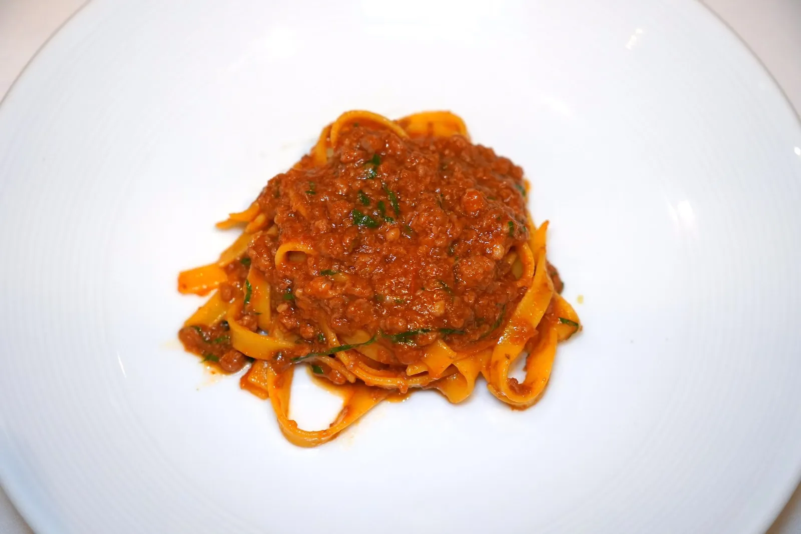 TAGLIATELLE ALLA BOLOGNESEHand-Made Tagliatelle, Bolognese Ragout, Tomato Sauce, Aged Parmesan Cheeseพาสต้าโฮมเมดเส้นแบนทัลยาเลียแตลเล่คลุกเคล้ามากับโบโลญเยเซ่รากูสูตรต้นตำรับจากแคว้นเอมิเลีย-โรมัญญารสชาติเข้มข้น นอกจากนี้ยังมีความอุมามิของมะเขือเทศและชีสพาเมซานอีกด้วย
