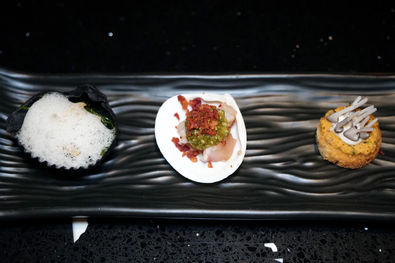 RAINY Marinated whelk w/ Chakram Salad, Coconut Foam & Charcoal Shell Day Catch Fish Aburi w/ Seasonal Vegetable Relish & Crispy Nama Ham House Made Brioche w/ Truffle Crab Roe & Mushroom เริ่มต้นมื้ออาหารด้วยอมูสบูชสามอย่างที่จะผลัดเปลี่ยนไปตามฤดูกาล สำหรับในฤดูฝนนี้ทางร้านนำเสิร์ฟมา 3 อย่างเป็นวันถุดิบจากท้องทะเลทั้งหมด ชิ้นเเรกทางซ้ายมือคือ “ข้าวเกรียบ” ที่มีสีดำของถ่านทำมาเป็นทรงเปลือกหอย ด้านในเป็นสลัดผักชะครามทอปด้วยหอยชักตีนเเละโฟมกะทิ ความมันของกะทิเข้ากันดีกับความเค็มของใบชะครามซึ่งเป็นพืชที่ขึ้นตามป่าชายเลน ส่วนหอยชักตีนให้เนื้อสัมผัสเคี้ยวหนึบตัดกันกับความกรอบของข้าวเกรียบสีดำด้านนอก (12/20) ชิ้นถัดมาเป็น “เนื้อปลาอังเกย” หรือปลากะพงเเดงหน้าตั้งที่เพื่อนของเชฟตกมาเองจากทะเลอ่าวไทยและส่งมาให้กับทางร้านทุกๆ 2 อาทิตย์ เชฟแนนใช้วิธีจัดการปลาแบบ Dasuijime จึงมั่นใจได้ว่าเนื้อปลายังคงสดอยู่ตลอด จากนั้นนำเนื้อปลามาอะบุริจนผิวด้านหนึ่งเริ่มสุก องค์ประกอบสีเขียวด้านบนคือยำผักปลัง ทอปด้วยนามะเเฮมทอดวางเอาไว้ด้านบน ชิ้นนี้เข้าใจว่าเชฟต้องการนำผักปลังมาใช้เพื่อเเสดงถึงเอกลักษณ์ความเป็นไทยเเต่เราคิดว่าเนื้อสัมผัสที่ได้ออกมาค่อนข้างสไลม์มี่มากไปจนกลบความดีงามของเนื้อปลาและนามะเเฮมไปพอสมควร (11/20) ชิ้นขวาสุดคือ “บริยอชบัน” กรอบๆ ด้านในสอดไส้ทรัฟเฟิลมาโยหอมๆ ทอปด้วยไข่ปูมันๆมีเห็ดชิเมจิเพิ่มมิติทางเนื้อสัมผัส ถือเป็นคำที่โดดเด่นที่สุดส่งท้ายอมูสบูชก่อนเข้าสู่อาหารจานหลัก (13/20)