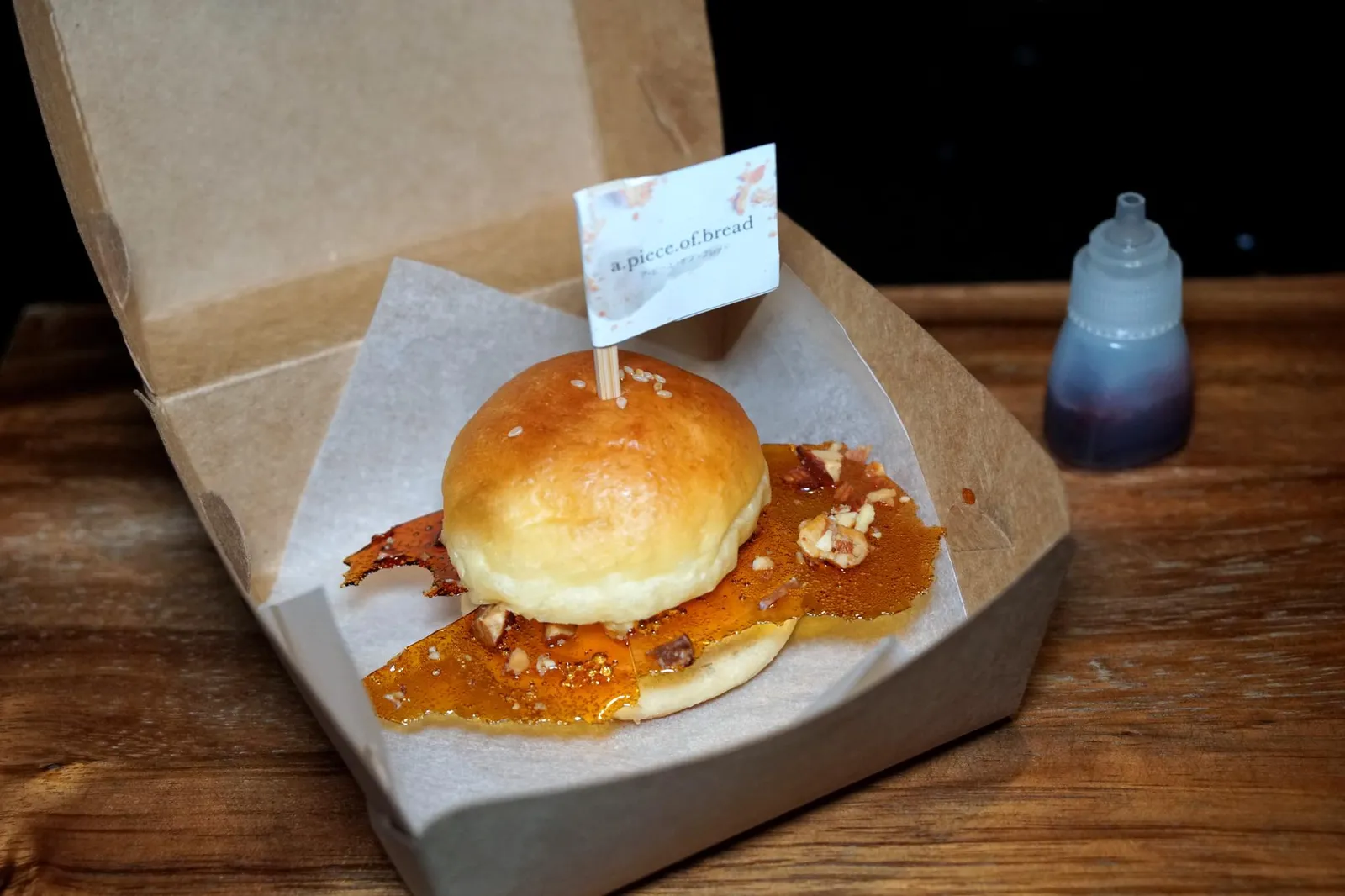 A PIECE OF BREAD Brioche bun w/ Bael Fruit Ice Cream, Hazelnut Praline & Roselle Sauce สำหรับขนมหวานวันนี้เชฟเลือกนำเสิร์ฟเป็น “อะพีซออฟเบรด (a.piece.of.bread)” ขนมปังแบรนด์ใหม่ที่เชฟสร้างขึ้นมาขายในช่วงปิดร้านจากสถานการณ์ปัจจุบันโดยในคอร์สนี้เชฟตั้งใจเลียนแบบมาจากเบอร์เกอร์เเต่เปลี่ยนองค์ประกอบต่างๆเพื่อทำให้เป็นของหวาน เริ่มจากขนมปังที่ใช้ประกบดูคล้ายเบอร์เกอร์คือ Housemade brioche bun ที่ทางร้านใช้เวลาทำถึง 2 วัน ไส้ด้านในคือไอศกรีมมะตูม แผ่นตรงกลางที่เลียนเเบบมาจากเบคอนคือฮาเซลนัทพราลีนทำมาจาก Burnt caramel มีรสชาติติดขมนิดๆเพื่อตัดความหวานของไอศกรีม ด้านบนโรยด้วยงาขาว ขวดซอสด้านข้างเลียนเเบบมาจากซอสมะเขือเทศเเต่เชฟเปลี่ยนมาใช้เป็นซอสกระเจี๊ยบเพื่อให้รสเปรี้ยวเเทน ขนมปังนุ่ม ฟู หอม ไอศกรีมมะนูมให้รสหวานเป็นเอกลักษณ์ ตัดด้วยความเปรี้ยวที่ลูกค้าเลือกเองได้จากการหยอดน้ำกระเจี๊ยบลงไป แผ่นคาราเมลไหม้ตรงกลางทำมาแอบแข็งไปเล็กน้อย โดยรวมถือว่าทำออกมาได้น่ารักดี อย่างไรก็ตามากรเสิร์ฟขนมปังปิดท้ายเป็นของหวานอาจดูหนักไปสำหรับเพื่อนๆบางคน (12/20)