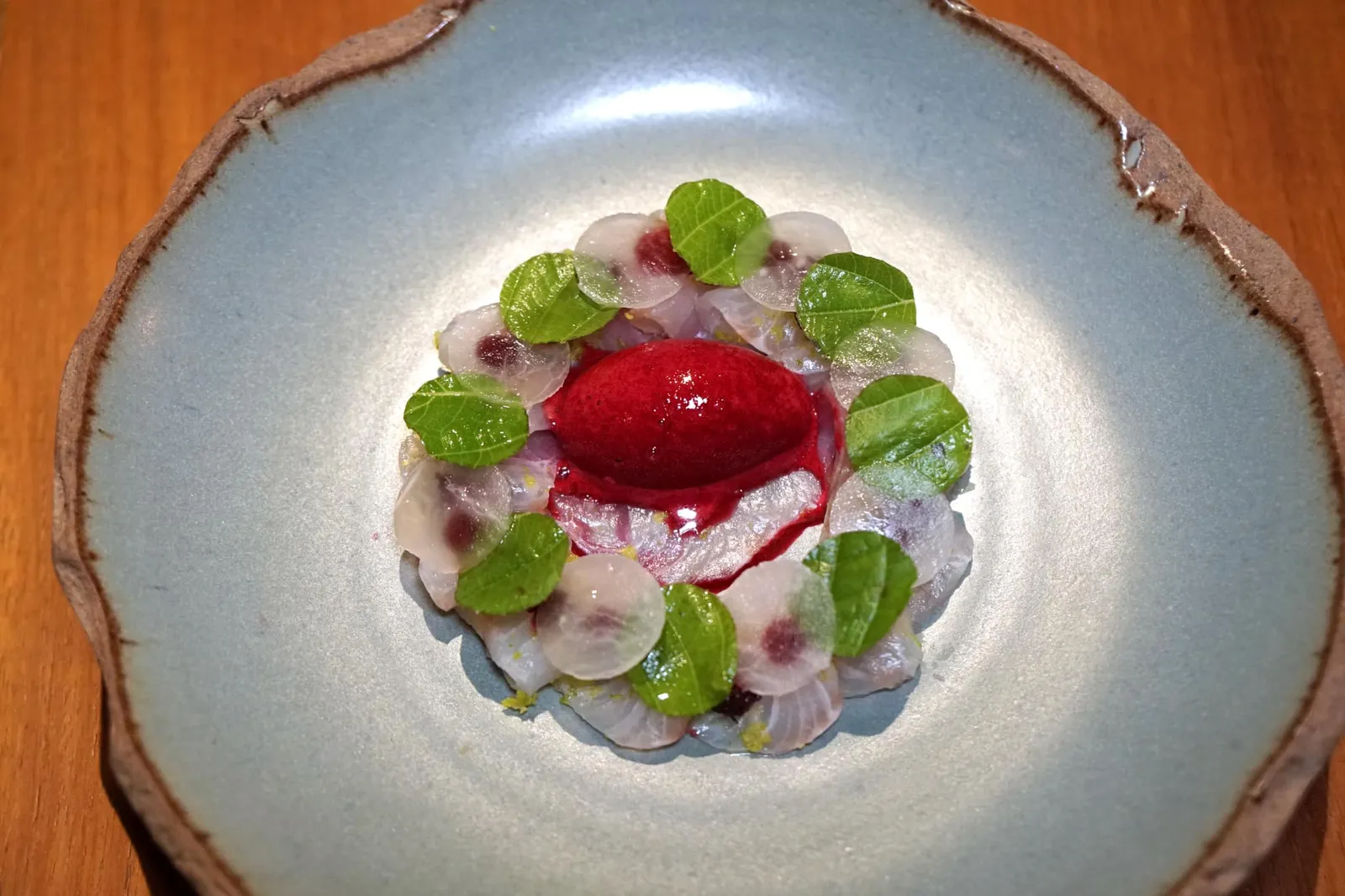 Phuket, a place where ocean and land meet Aged black king fish and mulberry จานแรกของฝั่ง 5 คอร์สเป็นตัวเเทนวัตถุดิบจากจังหวัดพังงาเช่นกัน ที่เห็นในจานคือ Cobia หรือ “ปลาช่อนทะเล” ที่เชฟนำไปห่อด้วยใบงาหอมหรือใบชิโสะเพื่อให้กลิ่นหอมเเทรกเข้าไปในเนื้อปลาแล้วจึงเเล่เป็นเเผ่นบางๆ จุดเด่นของเนื้อปลาช่อนทะเลคือเนื้อสัมผัสที่ค่อนข้างเฟิร์มแน่นเเต่ไม่เเข็ง แต่ด้วยความที่เป็นปลาเนื้อขาวทำให้รสชาติของเนื้อปลาไม่เด่นชัดมากนักเชฟ Jimmy จึงใส่องค์ประกอบด้านบนคือ Pickled turnip หรือหัวไชเท้าดองซึ่งจะมีความกรอบและเสริมรสเปรี้ยวนิดๆให้กับจานนี้ ข้างกันคือใบงาหอม จุดสีแดงที่ซ่อนอยู่ใต้เนื้อปลาคือ Mulberry หรือลูกหม่อน ซอร์เบท์สีเเดงสดตรงกลางทำมาจากลูกหม่อนผสมกับบีทรูทซึ่งจะมีความ Earthy เบาๆช่วยบาลานซ์รสเปรี้ยวของหัวไชเท้าดองไม่ให้เด่นแหลมจนเกินไป (17/20)