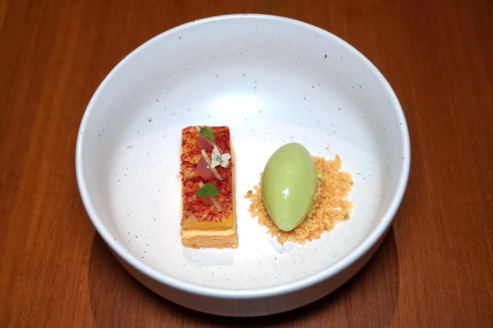Jewel of Phuket Phuket Pineapple and Makaewn ก่อนเข้าสู่อาหารหวานพนักงานจะนำเสิร์ฟ Pre-dessert เพื่อดับรสอาหารคาวจานก่อนหน้า เชฟเลือกใช้สับปะรดพื้นเมืองของจังหวัดภูเก็ตย่างจนกรอบ หอม ทั้งยังทำให้รสเปรี้ยวอมหวานของน้ำในตัวสับปะรดเด่นชัดมากยิ่งขึ้น ด้านล่างคือมูสสับปะรดเพิ่มความมัน และครีมมี่นิดๆ ข้างกันเป็นไอศกรีมทำจากใบเบซิลและมะแขว่นมีกลิ่นหอมเด่นเป็นเอกลักษณ์ ด้านล่างคือครัมเบิ้ลกรอบทำจากลูกกระบก (หรืออีกชื่อหนึ่งคืออีสานอัลมอนต์) ทานเเล้วให้ความสดชื่นคล้ายใบมิ้นตัดด้วยรสเปรี้ยวหวานของสับปะรด แปลก ไม่ซ้ำใคร (17/20)
