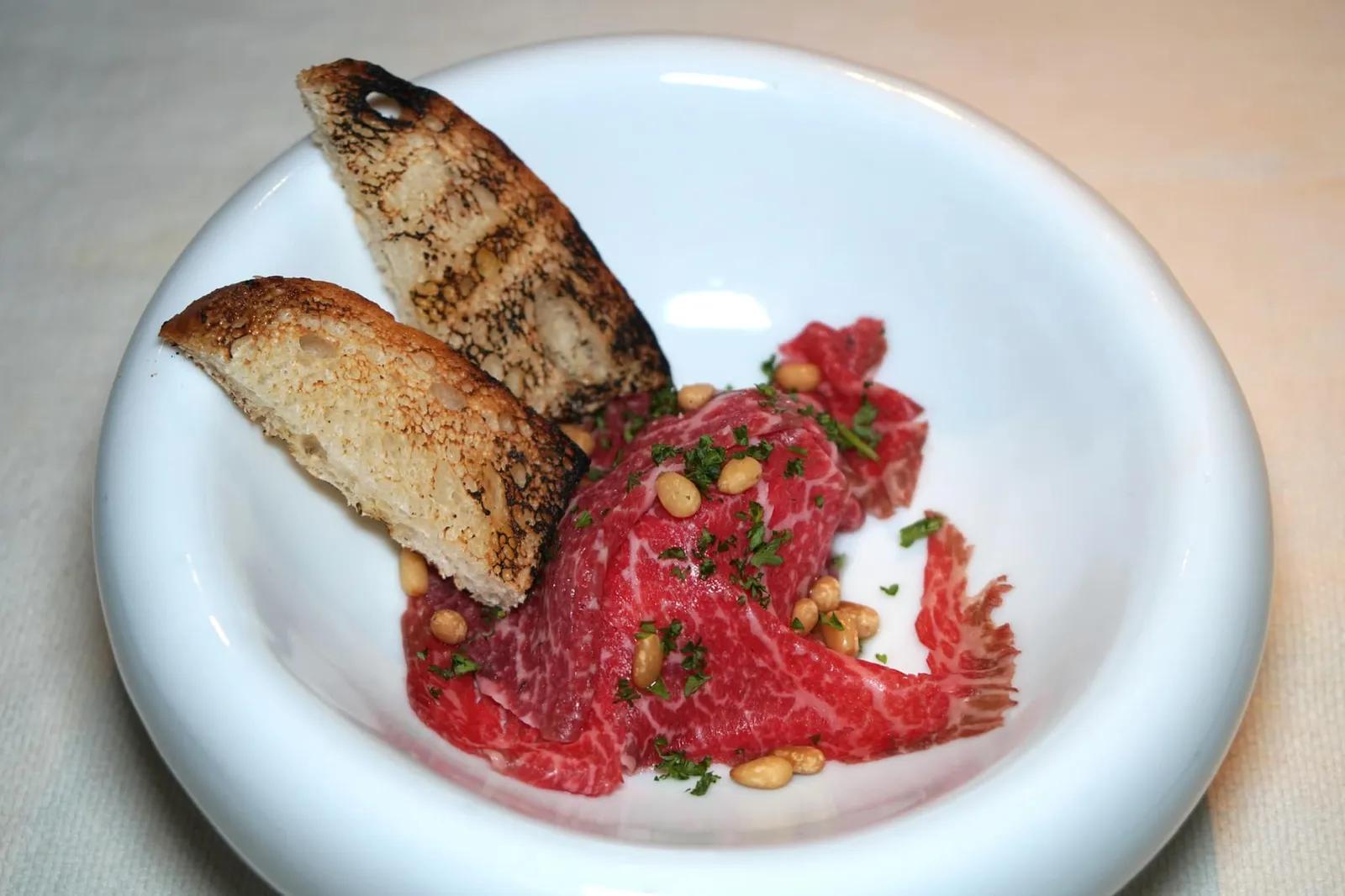 RANGERS VALLEY BLACK ONYX BEEF CARPACCIO Goat Cheese / Pinenuts / Smoked Olive Oil เมนูอาหารเรียกน้ำย่อยเชฟจานแรกเลือกใช้เนื้อวัว Black Onyx Beef หรือ Black Angus MB3+ จากฟาร์มวัว Ranger Valley ในประเทศออสเตรเลีย แล่มาเป็นชิ้นบางๆเป็นคาปาซโช่ รองด้านล่างด้วยชีสนมแพะซึ่งจะมีรสเฝื่อนเบาๆ จากนั้นเพิ่มมิติทางเนื้อสัมผัสโดยการใส่เมล็ดสนลงไป จากนั้นราดด้วยน้ำมันมะกอกรมควัน ตักลงบนขนมปังปิ้งอุ่นๆก่อนทาน (12/20)