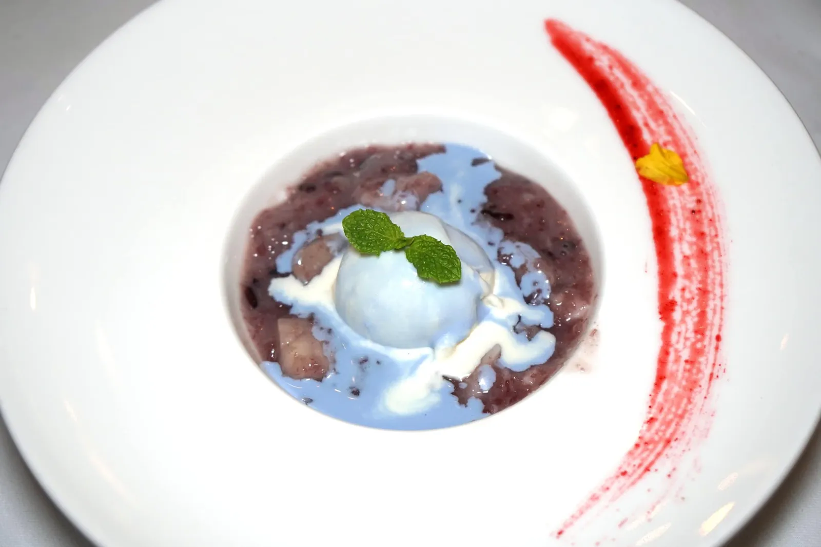 ข้าวเหนียวเปียกลําไย ไอศครีมมะลิ (220++) KAO NIEW PIEK LUM YAI JASMINE ICE CREAM Black sticky rice pudding topped with fresh longan and scented with Butterfly Pea flowers, Coconut cream served with Jasmine Ice Cream. ขนมหวานจานถัดมาคือข้าวเหนียวเปียกลำไย ทางร้านใช้ข้าวเหนียวดำราดด้วยน้ำกะทิ ทานคู่กับลำไยรสหวาน ไฮไลท์ของจานคือไอศกรีมกะทิที่มีกลิ่นหอมเด่นชัดมากๆ มีสีน้ำเงินสวยงามจากดอกอัญชัญ ตักไอศกรีม ลำไย ข้าวเหนียว เเละเนื้อมะพร้าวทานพร้อมกันเพื่อให้ได้รสชาติที่ดีที่สุด (14/20)