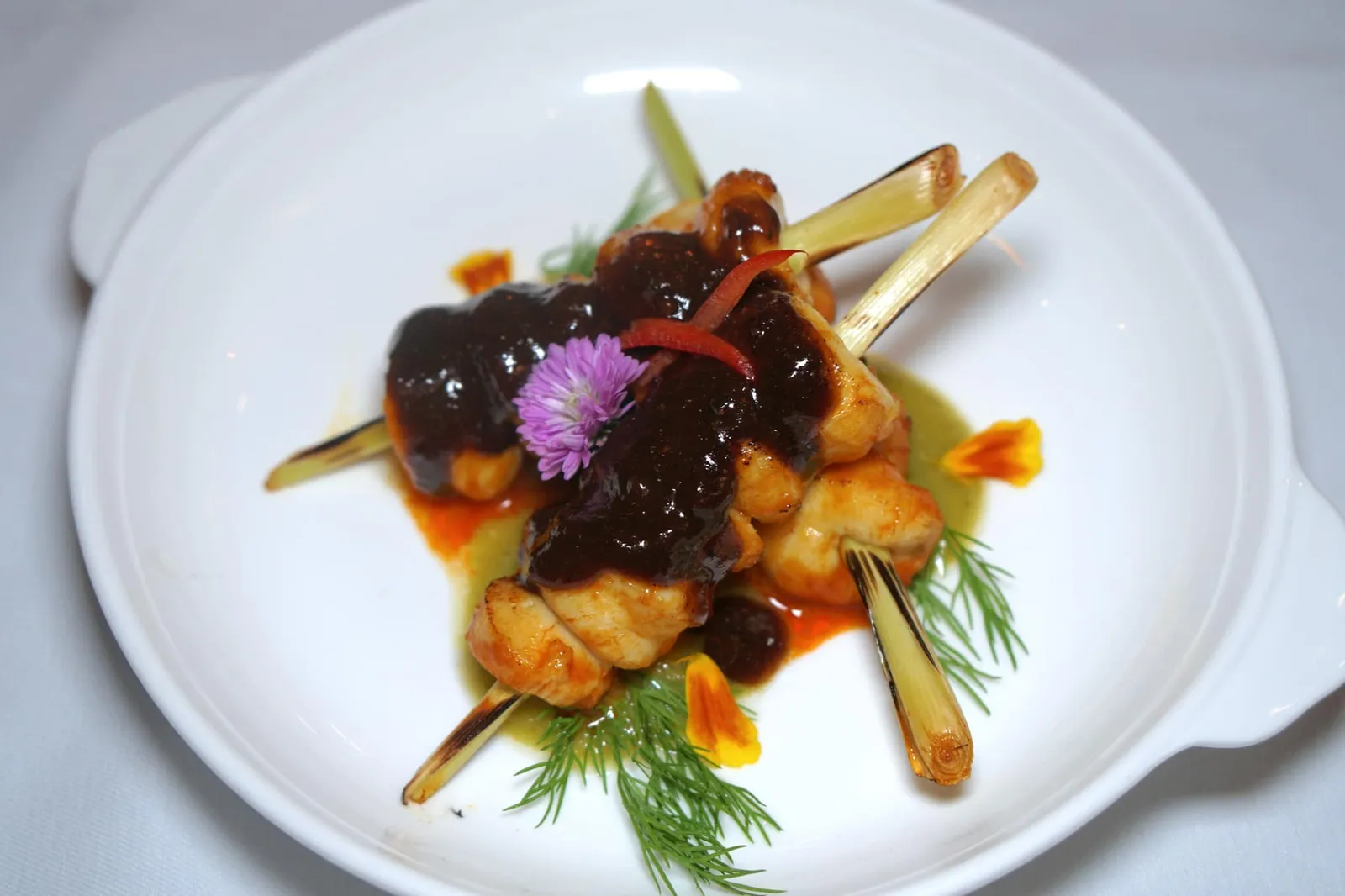 หอยเชลล์กระเทียมดำ อโวคาโด ซัลซ่า (420++) BLACK DIAMOND SCALLOPS AVOCADO SALSA Grilled Scallops - Southern Style marinated Herbs- Spicy Royal Project Farm Avocado Puree - Lampoon black Diamond Garlic - Sea Grapes. ไม่เคยสังเกตมาก่อนว่าเชฟนูรอมีหอยเชลล์เสียบตะไคร้ย่างขายในร้านด้วย เนื้อหอยเชลล์ผ่านการหมักกับสมุนไพรจนหอม จากนั้นย่างจนสุกพอดีจึงมีเนื้อสัมผัสนุ่มมากๆ ไม่มีกลิ่นคาว ซอสสีเขียวด้านล่างทำจากสมุนไพรและอโวคาโดให้รสชาติเผ็ดจัดจ้าน ทีเด็ดคือซอสด้านบนที่ทำมาจากกระเทียมดำจังหวัดลำพูน ที่สำคัญปริมาณที่ให้มาเทียบกับของว่างจานอื่นถือว่าเหมาะสมกับราคาและแบ่งกันทางได้ 3-4 คน (14/20)