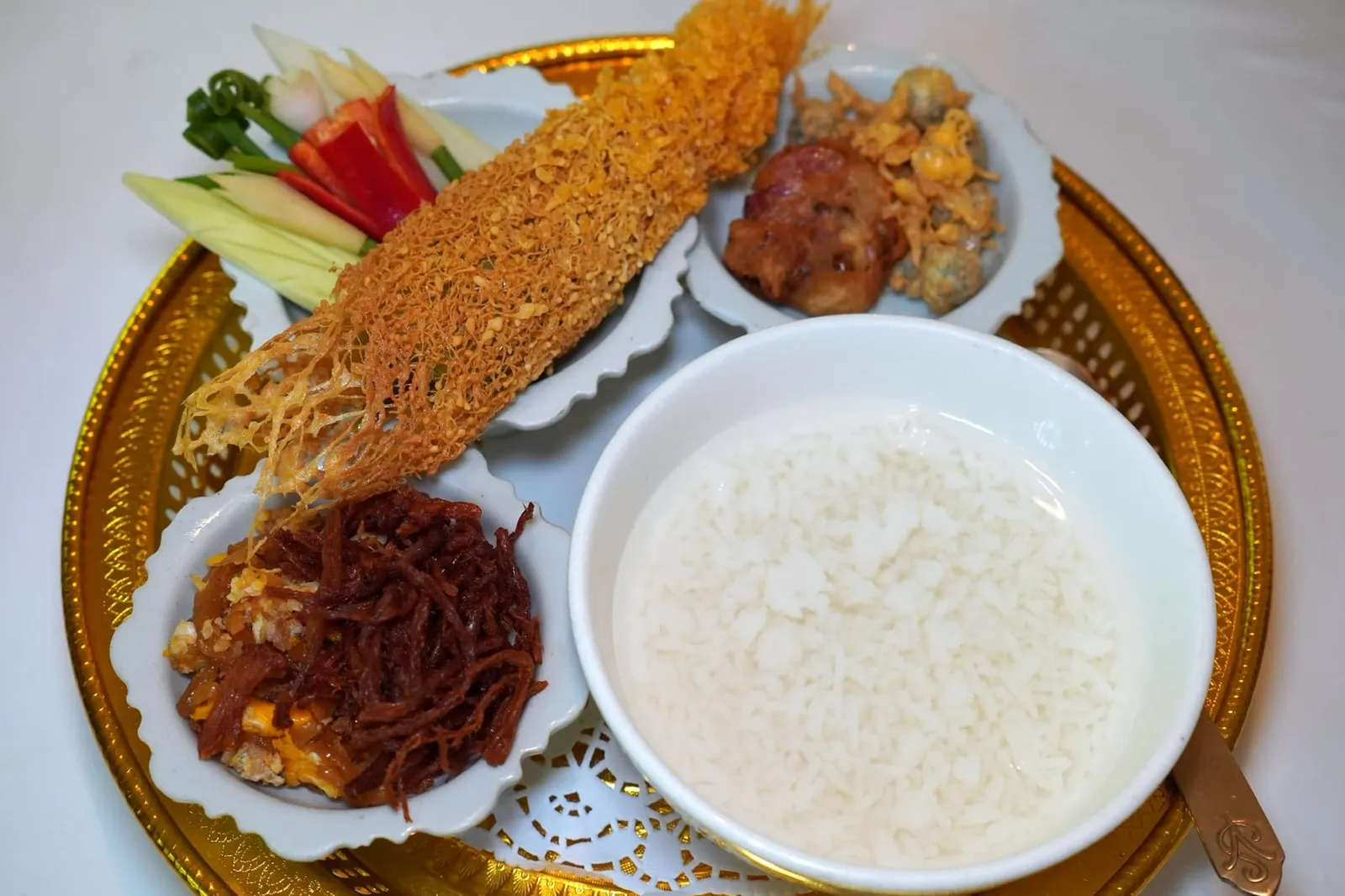 ข้าวแช่ชาววัง (450+) Thai summer dish ห้ามพลาดเมนูขึ้นชื่ออย่างข้าวแช่สูตรชาววัง (ปกติแล้วสูตรของที่นี่จะใช้ข้าวแช่ในน้ำดอกชมนาด ดอกมะลิ และกุหลาบมอญ) เสิร์ฟมาคู่กับเครื่องต่าง ๆ ทั้งลูกกะปิที่รสชาติหวานกลมกล่อม โดดเด่นกว่าร้านทั่ว ๆ ไป หอมแดงโทนสอดไส้ หมูฝอย ไชโป๊วผัดหวานและไข่แนม ยังมีพริกหยวกชิ้นโตสอดไส้หมูและกุ้ง นึ่งมาสุกพอดี จากนั้นโรยด้วยไข่ที่ได้จากการผสมไข่ไก่และไข่เป็ด ทอดออกมาเป็นแพหรือที่เราเรียกกันว่าหรุ่ม สีเหลืองทองสวยงาม ไม่อมน้ำมัน ขนาดยาวเลยขอบพาน และผักสดทั้งกระชายแกะสลักรูปดอกจำปี ต้นหอม แตงกวา พริกชี้ฟ้า และมะม่วงจนกลายมาเป็นเอกลักษณ์ของร้าน รสชาติโดยรวมถือว่าดีงามกว่าร้านอาหารไทยทั่วไปพอสมควรเลยทีเดียว (13/20)
