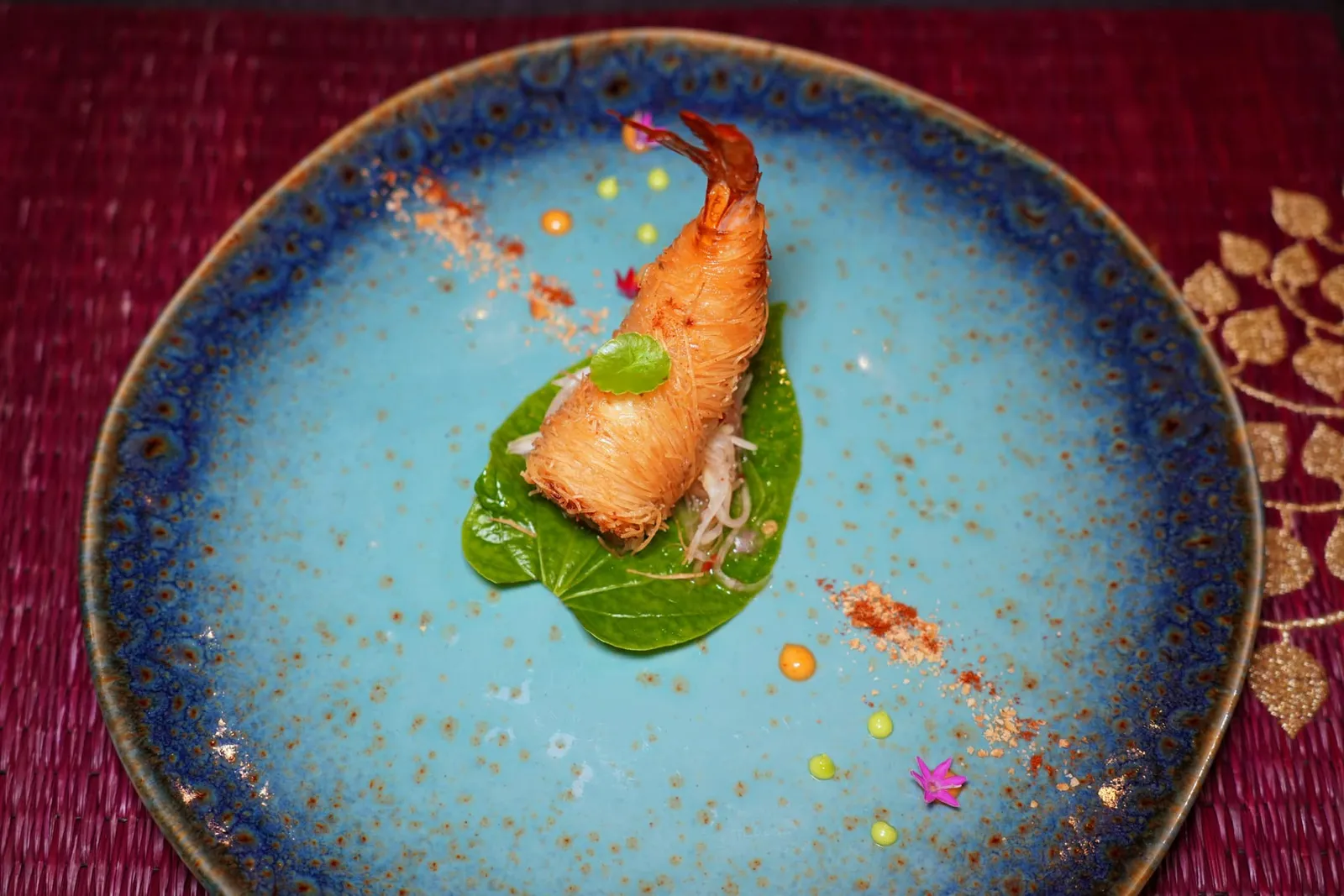 กุ้งโสร่ง King prawn with filo pastry ห้ามพลาดเมนู Signature Dish ที่มีติดอยู่ในรายการเมนูมานานอย่าง “กุ้งโสร่ง” ที่เสิร์ฟมาพร้อมกับ “ยำส้มกอ” เชฟห่อกุ้งโดยใช้ใช้วิธีโบราณโดยใส่หัวไชโป๊กรอบหวานเอาไว้ตรงกลาง รอบ ๆ เชฟเลือกที่จะเปลี่ยนชนิดของเส้นจากเส้นหมี่ขาวหรือหมี่เหลืองมาเป็นฟิโลแพสทรี่แบบตะวันตกแทนเพื่อให้ได้ความกรอบที่ชัดเจน ไม่แข็งกระด้าง ทั้งยังไม่อมน้ำมันอีกด้วย ส่วนยำส้มกอนั้นเป็นอาหารพื้นเมืองของชาวชองในจังหวัดจันทบุรี เชฟเล่าว่าด้วยความที่ชาวชองในอดีตโดนกองทัพของพระเจ้าตากบุกตีจนแตกพ่ายหนีเข้าไปในป่าทำให้อาหารของชาวชองมักไม่ผ่านไฟเพื่อไม่ให้ถูกข้าศึกเห็นได้โดยง่าย ด้านบนท็อปด้วยใบบัวบกน้ำ รอบ ๆ คือซอสโหระพามาโยสีเขียวอ่อนและซอสสไปซี่มาโยสีส้ม นอกจากนี้ยังมีองค์ประกอบของถั่วคั่วหอมและผงปาปริก้า จานนี้จบด้วยการตกแต่งด้วยดอกไม้จากสวนหลังบ้าน วิธีรับประทานให้ตักยำส้มกอที่มีรสชาติเปรี้ยวนำหวานแซมรับประทานคู่กันไปกับกุ้งโสร่งจะได้รสชาติครบทั้งเปรี้ยวหวานและเผ็ด ทั้งยังมีความกรอบเทียบกันกับกุ้งโสร่งจนเกิดมิติทางเนื้อสัมผัสที่ดีอีกด้วย (16/20)
