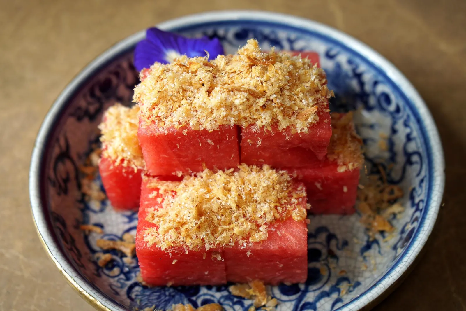 ปลาแห้งแตงโมบ้านใน Watermelon chunks with dried fish flakes and crispy shallots ปลาแห้งแตงโม เมนูที่มองจากภายนอกดูคล้ายกับเป็นอาหารไทยร่วมสมัยเเต่แท้จริงแล้วถือเป็นอาหารว่างชาววังที่มีบันทึกเริ่มต้นมาตั้งแต่สมัยอยุธยา แต่มาปรากฎหลักฐานชัดเจนในสมัยพระบาทสมเด็จพระพุทธยอดฟ้าจุฬาโลกมหาราชเมื่อครั้งทำพระราชพิธีสมโภชพระแก้วมรกตและฉลองวัดพระศรีรัตนศาสดาราม ทรงจัดเมนูปลาแห้งแตงนำเสิร์ฟพระสงฆ์กว่าสองพันรูป ควบคู่กับแกงพะแนง หมูผัดกุ้ง ไข่เจียว ลูกชิ้น มะเขือชุบไข่ทอด และกุ้งต้ม ทั้งยังเป็นอาหารว่างที่หมู่ขุนนางและพระเจ้าแผ่นดินนิยมทานกันช่วงฤดูร้อนอีกด้วย สำหรับ "ปลาแห้งแตงโม" ของร้านบ้านในถือเป็นเมนูที่โดดเด่นที่สุดในร้าน ขนาดที่เจ้าของร้านเคยเล่าให้เพื่อนฟังว่าถ้าได้เปิดร้านอาหารจะต้องนำปลาแห้งเเตงโมมาขึ้นไว้เป็นอย่างแรกเพราะเห็นคุณยายท่านทานทุกวัน ปกติคุณยายจะเเบ่งเครื่องปลาแห้งใส่กระปุกฝาเกลียวหรือกระปุกสุญญากาศเพื่อให้ถนอมความกรอบเอาไว้ได้นานครั้นจะทานก็นำแตงโมเเช่เย็นออกมาแล้วโรยเครื่องปลาแห้งลงไปทานเป็นอาหารทานเล่น หรือจะเอาเเตงโมมาจิ้มลงในปลาแห้งเเล้วทานคู่กับข้าวสวยก็รู้สึกชื่นใจไม่แพ้กัน สำหรับจานที่เราได้ทานในวันนี้ถือว่าทำรสชาติออกมาได้น่าประทับใจแตงโมสีแดงสดแช่เย็นหั่นออกมาเป็นชิ้นสี่เหลี่ยม โรยด้วยเครื่องปลาแห้งมาแบบพูนๆที่ด้านบนให้รสชาติหวานๆเค็มๆ ช่วยเรียกความสดชื่นก่อนเข้าสู่อาหารจานหลักได้เป็นอย่างดี แอบกระซิบว่าเครื่องปลาแห้งที่นี่อร่อยขนาดมีขายแยกในกระปุกสำหรับลูกค้าที่ต้องการซื้อกลับไปโรยเเตงโมทานที่บ้านเลยทีเดียว (14/20)