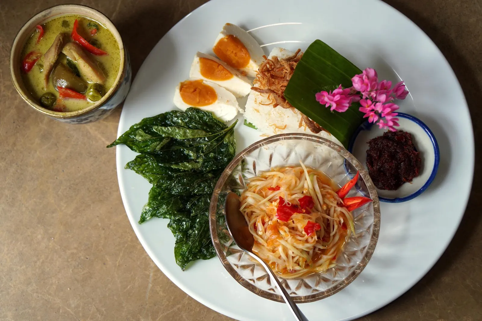 ข้าวมันส้มตำ Khao Man Som Tam อาหารไทยเป็นอาหารที่ทานข้าวร่วมกันกับเมนูกับข้าวหลายอย่าง เเม้จะมีรสชาติเเตกต่างกันออกไปเเต่พอทานสลับกันเเล้วจะเข้ากันเเละเสริมรสชาติกันให้อร่อยยิ่งขึ้น ข้าวมันส้มตำเป็นตัวอย่างของการทานอาหารเเบบสำรับไทยได้เป็นอย่างดี สมัยก่อนกับเเต่ละอย่างนะถูกจัดเเยกมาเป็นกับข้าว รับประทานร่วมกันบนโต๊ะหลายคน แต่สมัยนี้การรับประทานอาหารเปลี่ยนแปลงไป ทางร้านจึงนำกับข้าวทุกองค์ประกอบรวบรวมมาเป็นชุดสำหรับพอทานได้หนึ่งคน (14/20)
