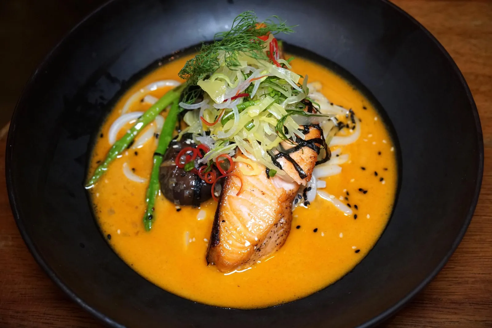 เส้นอุด้งปลาแซลมอนราดน้ำข้าวซอย (450++) Charcoal grilled salmon steak, yellow curry from Chiang Mai, Udon noodles อีกหนึ่งเมนูแนะนำของทางร้านคือเส้นอุด้งเหนียวนุ่มคลุกเคล้ากับน้ำมันงาและงาคั่วจนหอม เสิร์ฟมาคู่กับสเต๊กปลาแซลมอนที่พอทานเเล้วจะรู้ได้ทันทีว่าเป็น Farmed Norwegian Salmon ย่างถ่านมาสุกกำลังดี เนื้อเเน่น เเต่ไม่เเข็งกระด้าง จากนั้นพนักงานจะราดน้ำข้าวซอยสีส้มลงไปในจาน รสชาติน้ำข้าวซอยดูจะหวานไปเล็กน้อย ด้านบนคือยำที่มีผักหลายชนิดให้รสเปรี้ยวตัดกับความหวานของน้ำข้าวซอยได้เป็นอย่างดี จานนี้ต้องรีบสักหน่อยเพราะหากทิ้งไว้นานเนื้อเเละหนังของปลาเเซลมอนอาจจะนิ่มลงจากน้ำข้าวซอย (12/20)