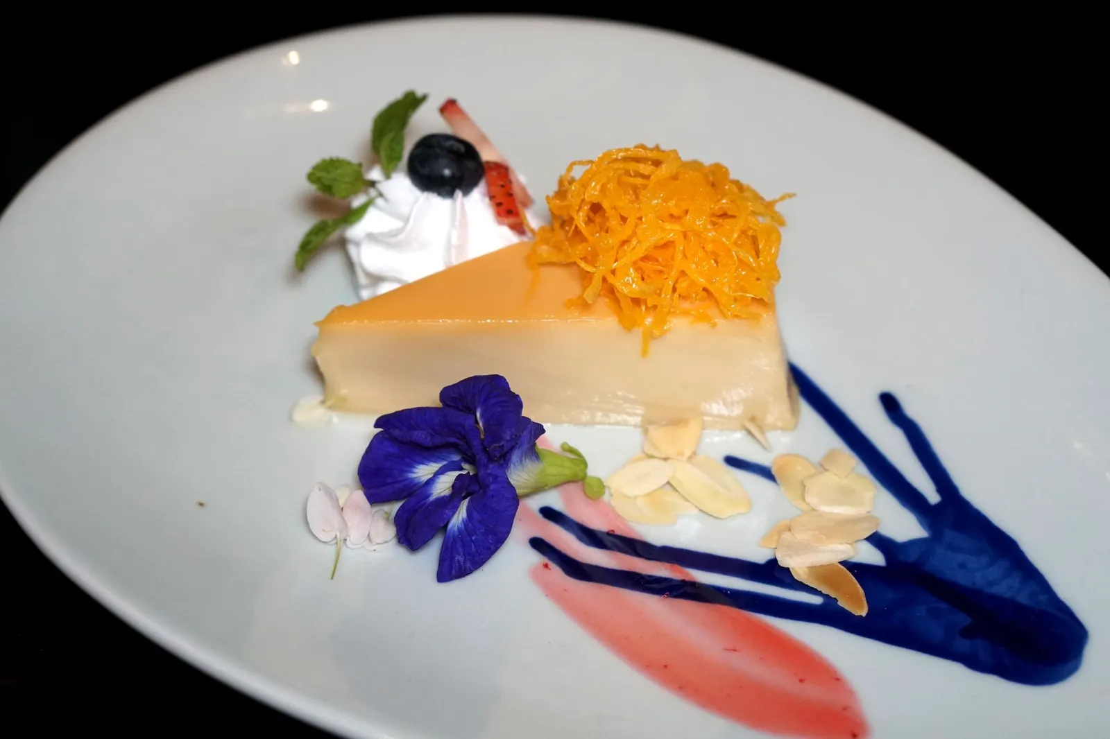 คัสตาร์ดมะพร้าว (210++) COCONUT FLAN An international Blue Elephant favorite: creamy caramelized coconut flan topped with Thai golden threads and almond flakes ไม่ใช่เพียง Chocolate Mousse เท่านั้นที่เชฟนูรอนำสูตรติดมาจากร้าน Blue Elephant สาขากรุง Brussels เเต่ยังมีขนมฟลานแบบฝรั่งที่เพิ่มความเป็นไทยโดยการใส่น้ำกะทิสดลงไป เนื้อฟลานเนียนนุ่ม หอมกลิ่นกะทิ ทอปด้านบนด้วยฝอยทอง เสิร์ฟมากับวิปปิ้งครีมที่ทางร้านตีเอง ถั่วอัลมอนต์ฝาน และผลเบอร์รี่ (13/20)