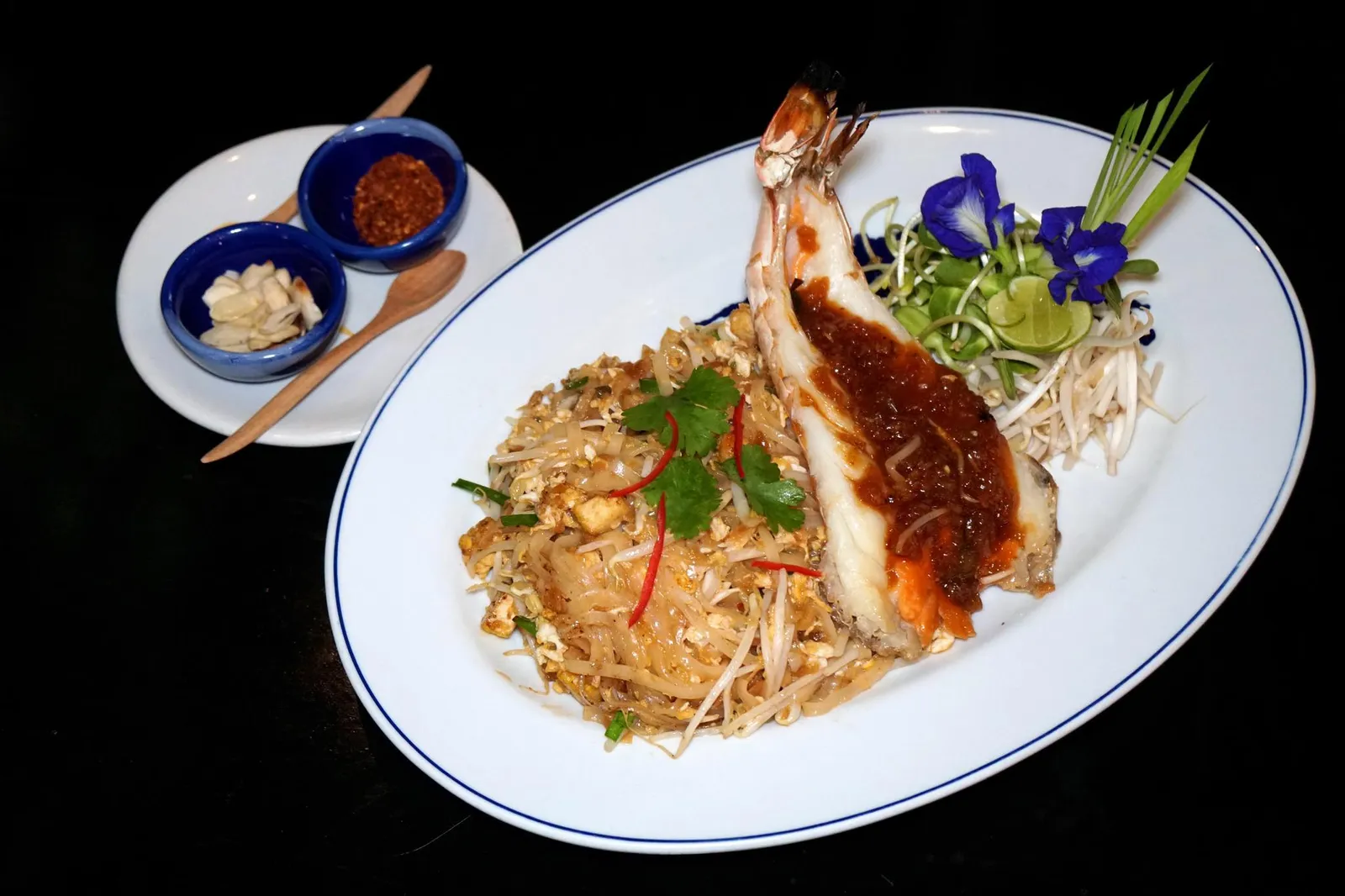 ผัดไทยกุ้งสดบลูเอเลเฟ่นท์ (780++) BLUE ELEPHANT TIGER PRAWN PHAD THAI “Chanthaburi” Rice Noodles - Fresh Deep Sea Tiger Prawns - Organic Egg ground roasted Peanuts – Tamarind - Banana Blossom - Kabok ใครที่อยากทานอาหารจานเดียวขอแนะนำสุดยอดผัดไทยซิกเนเจอร์ที่เชฟนูรอถึงขนาดนำชื่อร้านมาใส่เอาไว้ในชื่อเมนู เชฟเลือกใช้เส้นจันทน์จากจังหวัดจันทบุรีมาผัดกับไข่ออร์แกนิค ไฮไลท์คือการใส่กุ้งลายเสือตัวโตพร้อมซอสมะขามราดอยู่ด้านบน จานก็ใหญ่มากเเล้ว เเต่กุ้งก็ใหญ่ตามจานไปด้วย (14/20)
