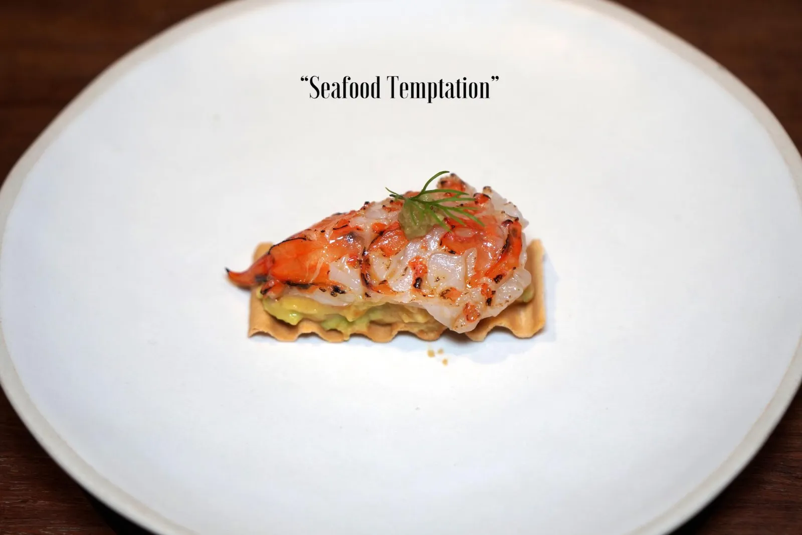 SEAFOOD TEMPTATION เริ่มต้นมื้ออาหารด้วยคอร์สอมูสบูชที่เชฟแนนนำเสิร์ฟแบบจัดเต็มถึง 5 อย่าง ! โดยคัดเลือกวัตถุดิบชั้นเลิศจากท้องทะเลไทย เริ่มต้นคำเเรกคือ “กุ้งลายเสือ” จากจังหวัดภูเก็ต เชฟแนนทอร์ชไฟเบิร์นที่ผิวด้านบนเพียงเบาๆทำให้เนื้อยังคงมีความนุ่มเด้งอยู่ ตรงกลางคือเลเยอร์ของอโวคาโดท้องถิ่นจังหวัดเชียงใหม่คลุกเคล้ากันมันกุ้งเพิ่มความหอมมัน ซอสสีเขียวด้านบนคือโคโชสไตล์ญี่ปุ่นที่เชฟเปลี่ยนจากวาซาบิแบบดั้งเดิมมาใช้เป็นดอกข่าของไทยแทนเพื่อให้รสเผ็ดเบาๆตัดกับความหวานของเนื้อกุ้ง ที่สำคัญคือกลิ่นดอกข่าที่หอมโดดเด่นมากๆ ด้านล่างคือแผ่นแครกเกอร์กรอบทำมาจากโคจิช่วยเพิ่มมิติทางเนื้อสัมผัสตัดกันกับเนื้อกุ้ง (14/20)