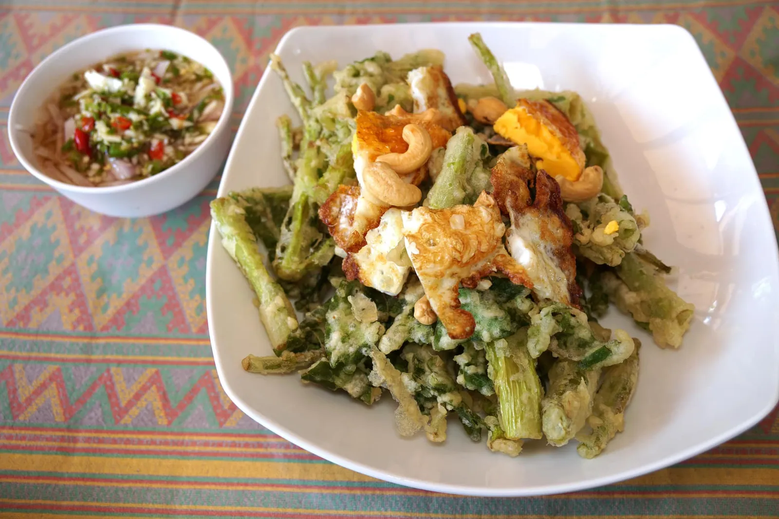 ยำผักบุ้งกรอบ (100) Hot and spicy morning glory salad คุณหนอเเนะนำเมนูนี้ให้เราเนื่องจากเป็นจานที่วัยรุ่นเค้าชอบทานกัน 😂 ผักบุ้งสดๆ ล้างน้ำจนสะอาด แล้วแป้งเเล้วทอดจนกรอบ ทอปด้วยไข่ดาวหั่นเป็นชิ้นๆ มีเมล็ดมะม่วงหิมพานต์เพิ่มมิติความกรอบ ราดน้ำยำรสชาติจัดจ้านลงไป … ลืมบอกไปว่าในน้ำยำยังมีทั้งกุ้งเเละหมึกอยู่ด้วยนะ (12/20)