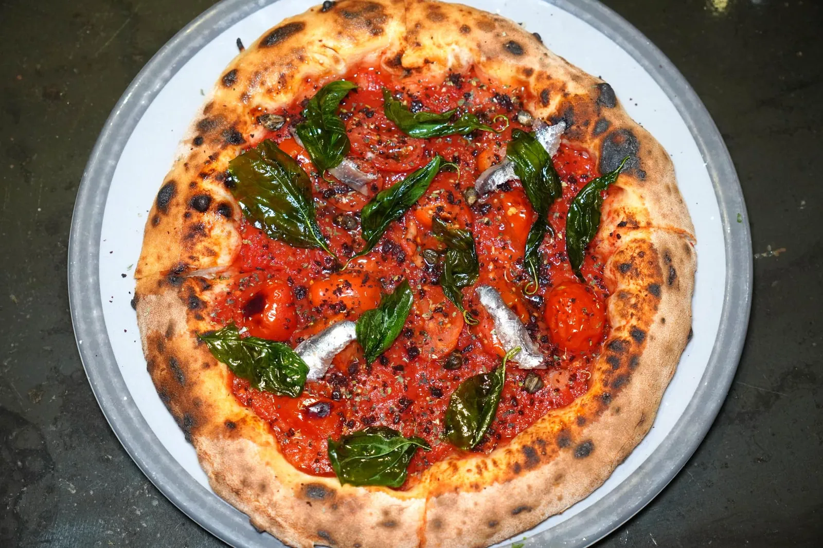 LA RITROVATA (dedicated to my father Stefano) San Marzano DOP tomato purée, “Piennolo” DOP tomatoes from the area of Vesuvius, dried capers, powder of Caiazzo black olives, Cetara anchovy fillets, garlic-infused olive oil, fried basil The Ritrovata เป็นพิซซ่าที่เชฟรังสรรค์ขึ้นเพื่อเป็นเกียรติให้แก่คุณพ่อของเขา Stefano โดยการเลือกใช้มะเขือเทศ San Marzano DOP เตรียมมาในรูปแบบของ Purée ละเลงไปจนทั่ว จากนั้นผสมผสานเข้ากันกับรสชาติของมะเยือเทศ Piennolo DOP ที่เจริญเติบโตบนดินพูเขาไฟ Vesuvius จนได้ความเปรี้ยวอุมามิที่ซับซ้อน ยังมี Anchovies ซึ่งเป็นสินค้าขึ้นชื่อระดับโลกจากเมือง Cetara ให้รสชาติที่เค็มกลมกล่อม เติมแต่งกลิ่นด้วย Capers แห้งและมะกอกดำท้องถิ่นของเมือง Caiazzo เทราดน้ำมันมะกอกที่ Infused ด้วยกระเทียมลงไปแล้วเพิ่มคมิติทางเนื้อสัมผัสด้วยความกรอบของใบ Basil ทอดใส่เอาไว้ที่ด้านบน (16/20)