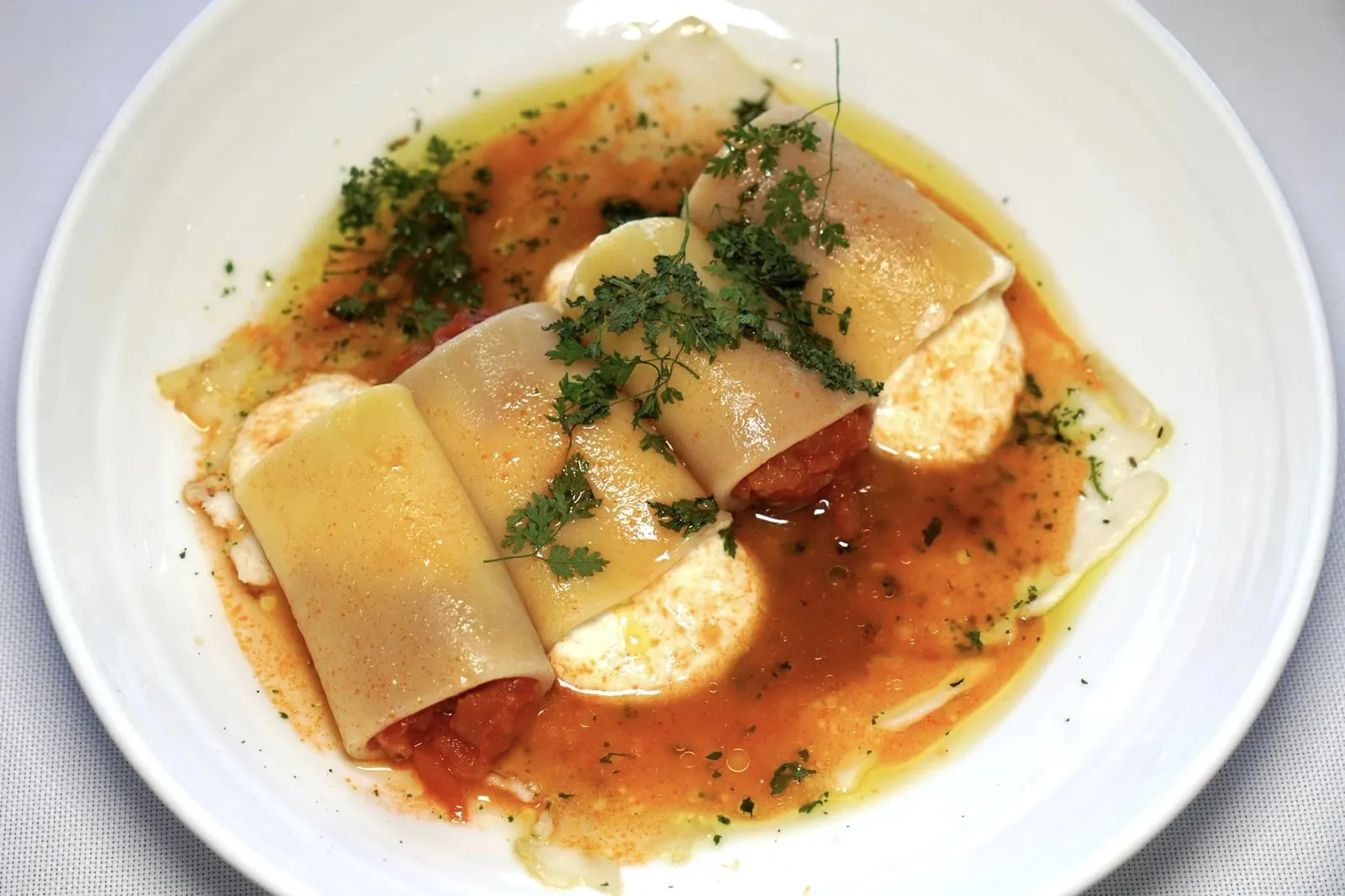 PACCHERI RIPIENI DI POMODORI AL FORNO E BURRATA (27 €) Paccheri pasta filled with baked tomatoes and burrata cheese | warm sea bream carpaccio with aromatic herbs | tomato broth Paccheri เป็นพาสต้าทรงกระบอกขนาดใหญ่ ด้านในสอดไส้มะเขือเทศอบและชีส Burrata วางสลับด้านกันเพื่อความสวยงาม เมื่อแรกเตี้ยวจะสัมผัสได้คชถึงความอุมามิและครีมมี่ ด้านล่างรองด้วยเนื้อปลา Orata ซึ่งเป็นปลาในกลุ่ม Sea Bream จากภูมิภาค Sardinia และสมุนไพรนานาชนิด จากนั้นเชฟจึงเทราดซุปใสที่เตรียมมาจากมะเขือเทศลงไปทั่ว ๆ จาน (13/20)