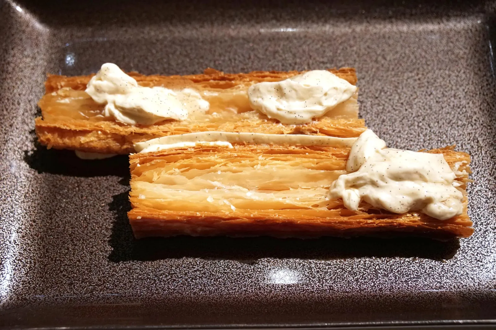 'Open' mille-feuille with Tahitian vanilla Mille feuilles ouvertes à la vanille de Tahiti Trois couches de pâte feuilletée intercalées de crème légère à la vanille de Tahiti, elle-même accompagnée d'une eau de vanille maturée avec les gousses 48 heures. บนจานสี่เหลี่ยมผืนผ้ารูปทรงคล้ายหนังสือเป็น Classic Signature Dessert ของ Restaurant Guy Savoy ชื่อของเมนูนี้คือ Millefeuille à la vanille เสิร์ฟมาในรูปแบบ “โอเพ่น มิลเฟย” เชฟเล่าว่ามิลเฟยวานิลลาที่นี่ Made to order และถูกจัดเตรียมในระดับ À la minute หรือแทบจะ À la seconde เลยก็ว่าได้ แป้งมิลเฟยถูกแบ่งออกมาเป็น 2 เลเยอร์ (ถ้าสั่งเป็นอลาคาร์ทจะเสิร์ฟมาถึง 3 เลเยอร์) ให้ความเบา ฟู กรอบ ดีที่สุดเท่าที่เมนูคลาสสิคจานหนึ่งจะสามารถถูกรังสรรค์ขึ้นมาได้ ด้านล่าง ด้านบน และระหว่างชิ้นของแป้งมิลเฟยเป็นตาฮิติวานิลลาครีมที่ใช้เวลาในการทำนานกว่า 48 ชั่วโมงให้ความหอมมันที่พอเหมาะ รสชาติออกหวานไม่เด่นจนเกินไป แนะนำให้ตักครีมเยอะ ๆ สัมผัสถึงรสชาติที่แท้จริงของเมนูนี้ (18/20)