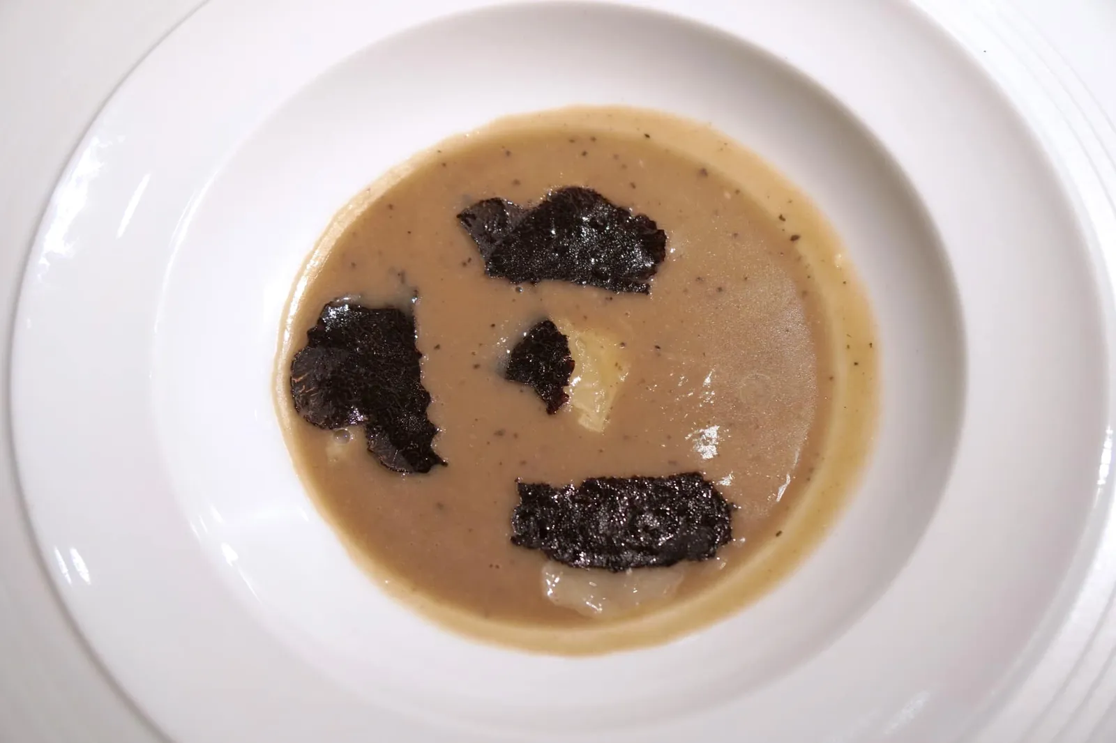 Artichoke soup with black truffle; layered truffled mushroom brioche and more... Soupe d'artichaut à la truffe noire, brioche feuilletée aux champignons et truffes, et encore plus… Artichoke soup, black truffle and Parmesan shavings; layered mushroom brioche spread with truffle butter. องค์ประกอบแรกของจานคือซุปร้อน ๆ ที่ได้จากการนำอาติโชคไปผ่านการต้มในน้ำเกลือทะเล จากนั้นนำไปเคล้ากับ Truffle jus จนได้เป็นซุปเข้มข้น มีกลิ่นหอม เนื้อสัมผัสเนียนละเอียดโดยไม่มีส่วนผสมของครีมหรือนมใด ๆ ปนมา องค์ประกอบสีขาวด้านบนคือพาเมซานชีส มีรสเค็มและมันเบา ๆ ตัดกับรสครีมมี่ของอาติโชคเเละอโรม่าของทรัฟเฟิลได้อย่างไร้ที่ติ ปิดท้ายด้วยการขูดทรัฟเฟิลสไลด์ทอปลงไปด้านบน บอกเลยว่าอโรม่าความหอมอันเป็นเอกลักษณ์ของทรัฟเฟิลสามารถลอยมาเเตะจมูกเราตั้งเเต่ตอนที่พนักงานยังนำซุปมาวางไม่ถึงที่โต๊ะเลยด้วยซ้ำ (20/20)