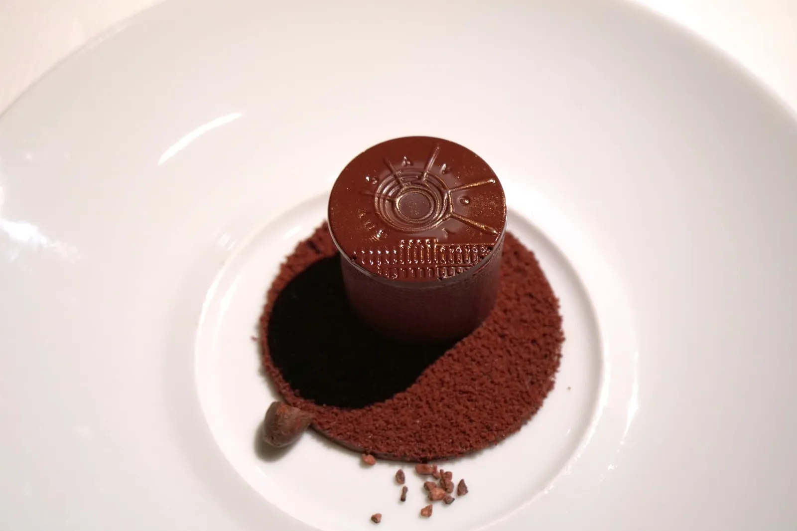 Pure chocolate Purement chocolat A crisp tube concealing a dark chocolate mousse, cacao sorbet and a sea salt biscuit, served with a warm chocolate sauce. สุดยอดเมนูขนมหวาน Signature Dish ยุคปัจจุบันของ Restaurant Guy Savoy อย่าง “ช็อกโกแลตบริสุทธิ์” เกิดจากความร่วมมือของเชฟ Guy Savoy และ Pastry chef ประจำร้าน Matthieu Carlin เป็นเมนูที่แสดงออกถึงเทคนิคการปรุงอาหารชั้นสูงและเทคนิคการผลิตเหรียญไปพร้อม ๆ กันอันเนื่องจาก Restaurant Guy Savoy ปัจจุบันนั้นตั้งอยู่บนชั้นสองของ Monnaie de Paris หรือโรงกษาปณ์แห่งกรุงปารีสนั่นเอง เชฟ Matthieu เลือกใช้ Valrhona Guanaja Chocolate อันเนื่องมาจากเหตุผล 2 อย่างคือการที่ช็อกโกแลตชนิดนี้เป็นชนิดโปรดของเชฟ Guy Savoy ยิ่งไปกว่านั้นขนม Chocolate mousse ที่เสิร์ฟปิดท้ายในรถขนมหวานก็ใช้ Valrhona Guanaja Chocolate เป็นองค์ประกอบหลักเช่นกัน นอกจากนี้เชฟ Matthieu ยังบอกว่าช็อกโกแลตชนิดนี้มีความหนืดในระดับที่พอเหมาะ สามารถแนบสนิทไปกับแบบพิมพ์ เชฟได้ใส่ Cocoa butter ลงไปเล็กน้อยเพื่อเสริมให้ขอบมีความเนียนเรียบและไม่ให้เกิดฟองขึ้นในกระบวนการพิมพ์ลาย หลังจากขนมเวอร์ชั่นแรกเป็นการผสมผสานรสชาติของช็อกโกแลตเข้ากับน้ำผึ้ง ในเวอร์ชั่นปัจจุบันเชฟจึงตั้งใจแสดงถึงความบริสุทธิ์ของช็อกโกแลตในเนื้อสัมผัสและอุณหภูมิที่แตกต่างกันหลายองค์ประกอบคือ Sorbet chocolat, Mousse légère chocolate, Gelée de cacao, Chocolate biscuit, Opaline chocolat, Croquette au chocolate, Pièces en chocolate และ Finiton et dressage (20/20)
