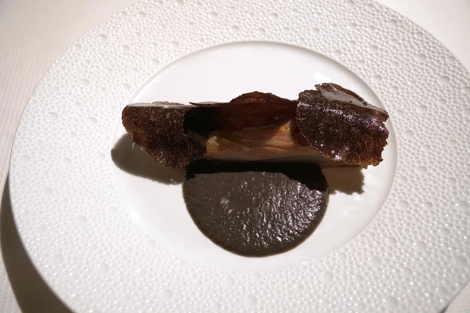 Confit chicory leaves interlaced with foie gras, dress with truffle Feuilles d'endives confites, du foie gras «intercalé», de la truffe autour Alternating layers of foie gras and chicory braised in poultry jus, cooked à la plancha and seasoned with a truffle jus. จานถัดมาคือ “ฟัวกราส์และใบชิโครี่” โดยใบชิโครี่ถูกนำไปกงฟีและตุ๋นในน้ำสต็อกสัตว์ปีกจนนุ่ม จากนั้นจึงนำไปปรุงในรูปแบบ À la plancha หรือย่างจนผิวด้านนอกเกรียมนิด ๆ มีกลิ่นหอมเพิ่มเติมขึ้นมา จากนั้นจึงห่อฟัวกราส์ตับเป็ดเอาไว้ด้านใน ความนุ่มละมุนของฟัวกราส์ให้แตกต่างออกไปจากความนุ่มของชิโครี่ ในด้านรสชาติจัดว่ามีความขมปนมาด้วยมากไปเพียงนิดเดียว (19/20)