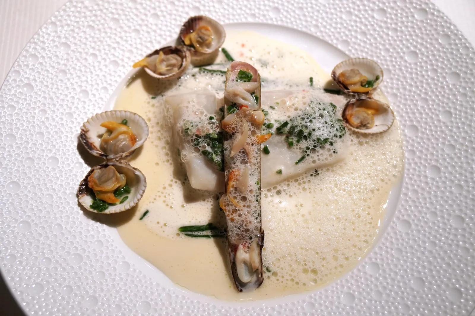 Oven-baked John Dory with a delicate shellfish parcel Saint-Pierre au four, un sac éphémère de coquillages Lightly baked John Dory with a ravigote flavoured with sea herbs; shellfish en papilote, 'marinière' jus with mushrooms. เนื้อปลาจอห์น โดรี่ ผ่านการอบมาเพียงชั่วครู่จึงมีเนื้อสัมผัสนุ่มลิ้นมาก ๆ จนเกือบจะละลายได้ในปาก เป็นความเพอร์เฟคของเนื้อสัมผัสของปลาชิ้นหนึ่งที่เรายังจดจำมาได้จนถึงตอนนี้ ด้านบนทอปด้วยหอยหลอดเสิร์ฟมาในฝาของตัวเอง ด้านล่างมี Chive หอยกาบข้าง ๆ กันมีความหนึบได้ระดับ สังเกตได้จากการที่เนื้อหอยไม่หดตัวลงแม้แต่น้อย การที่เชฟกัก Shellfish jus เอาไว้ทำให้สามารถในจานมีอโรม่าของหอยอยู่เต็มเปี่ยม พืชทะเล Salicornia ช่วยดับกลิ่นคาวและกลิ่นเฉพาะตัวของหอยได้หมดจด ความนุ่มของเนื้อปลาและความหนึบของเนื้อหอยจะทำให้เกิดมิติทางเนื้อสัมผัสแตกต่างกันออกไปในแต่ละคำ ซอส Marinière ทำมาจาก Saint-Pierre Jus หรือน้ำจากตัวปลาเองให้กลิ่นอายของทะเล ทั้งยังมีรสชาติออกเปรี้ยวนิด ๆ จาก Beurre Blanc และมีความเป็นไอโอดีนจากพืช Salicornia มีความ Earthy เบา ๆ จากเห็ด หากสังเกตดี ๆ จะพบ Lime Caviar เคี้ยวกรึบแอบอยู่ใน Salicornia ถือเป็นอีกหนึ่งจานที่เชฟ Guy Savoy แสดงให้เราเห็นถึงความซับซ้อนและหลากหลายทั้งในรสชาติ กลิ่น เนื้อสัมผัสในอาหารเพียงจานเดียว (20/20)