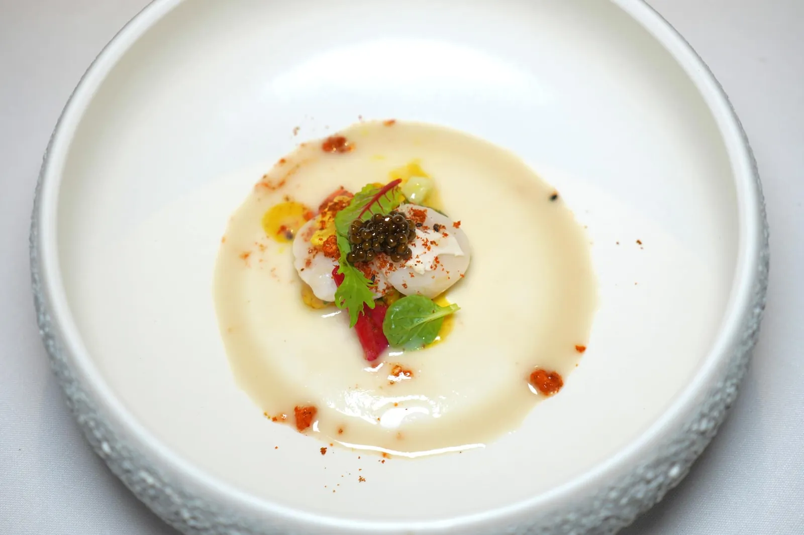 SCALLOPS, CAULIFLOWER mantis shrimp juice, roasted sesame and Kaluga Amur caviar หอยเชลล์เนื้อนุ่ม ๆ เสิร์ฟมาให้เข้ากันกับความกรอบของดอกกะหล่ำ เชฟเสริมความหอมด้วยการโรยพริกญี่ปุ่น Tōgarashi ลงไป นอกจากนี้ยังมีความเค็มเบา ๆ ที่ได้จาก Kaluga Amur Caviar อีกด้วย ส่วนสีขาวรอบ ๆ คือซอสที่เตรียมขึ้นมาจากกั้งนั่นเอง (16/20)