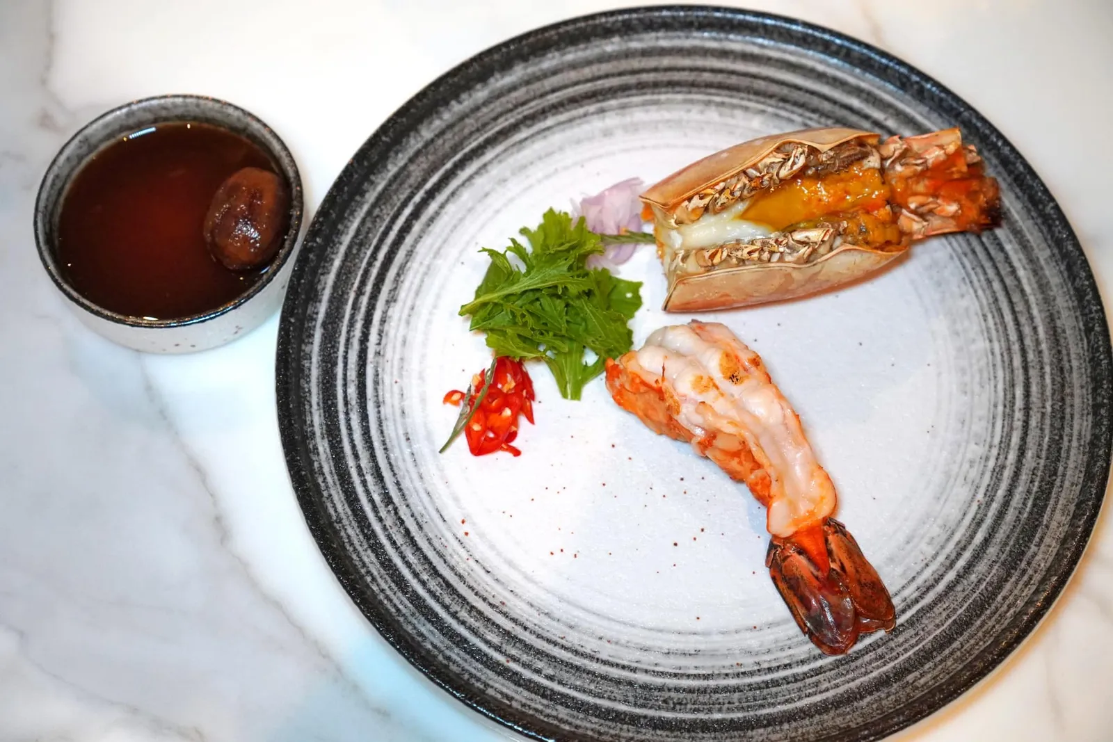 เลิศรสลงสรง (กุ้งย่างน้ำปลามะกอก) (~112 ปี) Grilled River Prawn with Fermented Thai Olive Sauce ไฮไลท์ของมื้อนี้ต้องยกให้กับเมนูที่ได้รับแรงบันดาลใจมาจากหนังสือ “เมื่อคุณตาคุณยายยังเด็ก” ประพันธ์โดยทิพย์วาณี สนิทวงศ์ ณ อยุธยา เล่าถึงราชสกุลสนิทวงศ์ ว่ากันว่ากรุงเทพในสมัยก่อนมีความอุดมสมบูรณ์ขนาดหาจับกุ้งแม่น้ำได้ด้วยมือเปล่า เชฟนำไปย่างจนสุกพอดีเสิร์ฟมาคู่กับหัวกุ้งและมันกุ้งเยิ้ม ๆ ปรุงรสด้วยพริกแดง หอมแดง และน้ำปลามะกอกซึ่งเป็นเมนูที่เคยพบได้ทุกครัวเรือนในกรุงเทพสมัยก่อนแต่กลับสูญหายไปอย่างรวดเร็วในยุคปัจจุบัน (14/20)
