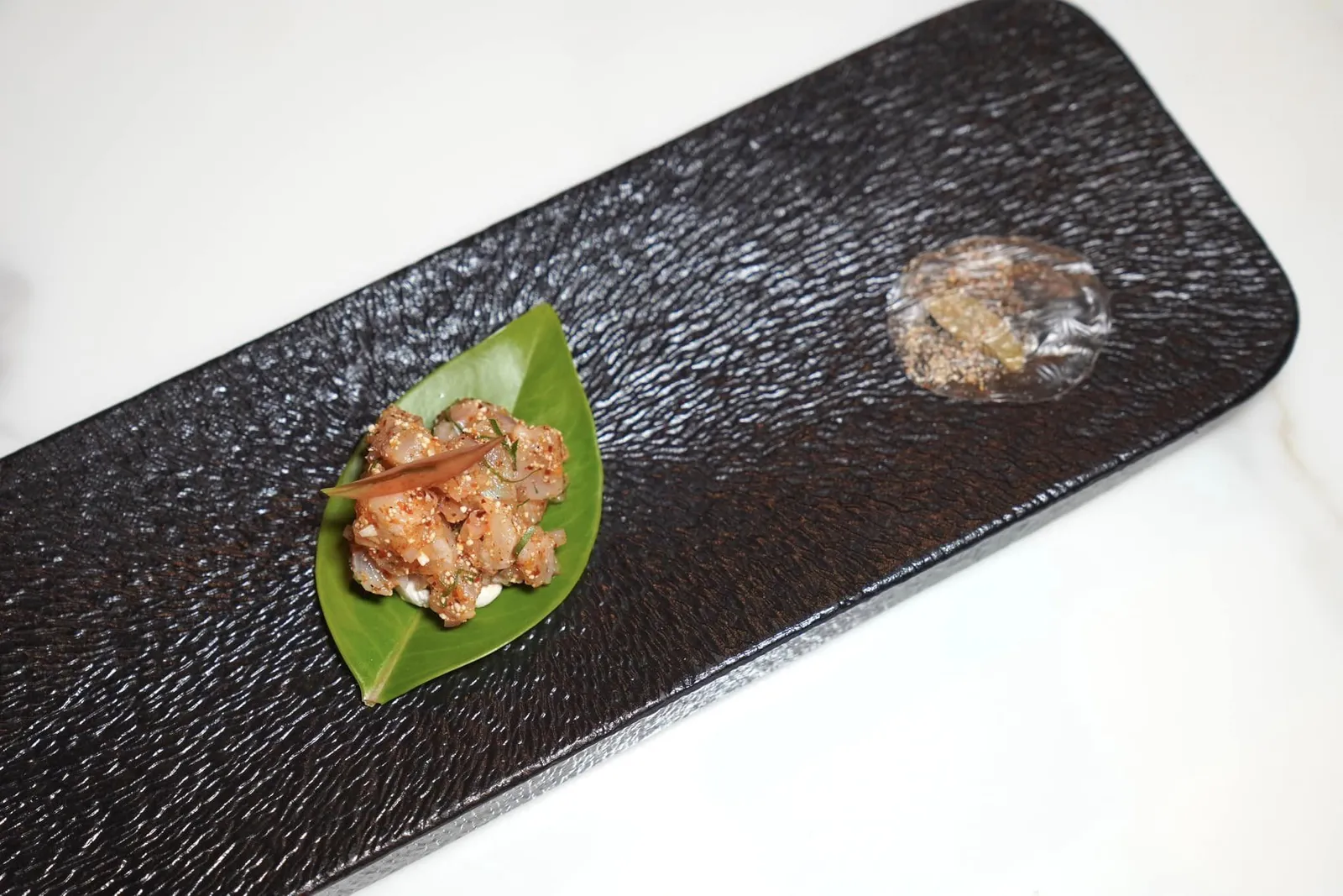 มัสยาส้มใบ (ลาบปลากระพงแดง) (~724 ปี) Red Seabass Spicy Salad หนึ่งในเมนูที่ถอดความมาจากหนังสือ From Marco Polo to McDonald's: Thai cuisine In Transition เขียนโดย Penny Van Esterik โดยตัวเชฟต้องการเล่าถึงเมนูในแถบ Yunnan ประเทศจีนที่เชื่อกันว่าเป็นต้นกำเนิดของลาบอย่างไทยนำเสนอเป็นปลากระพงแดงสับมาเกือบละเอียดจนได้เนื้อสัมผัสที่นุ่มละมุน จากนั้นนำไปยำกับเครื่องลาบรสชาติจัดจ้านและใส่ข้าวคั่ว มะแขว่น และพริกคั่วลงไปด้วย ด้านล่างรองด้วยใบชะมวงเสริมด้วยน้ำมะม่วงเยาให้รสเปรี้ยวแทนมะนาว ข้างกันคือแผ่น Cracker กรอบเตรียมมาจากน้ำมะม่วงเบาอีกเช่นกัน (13/20)