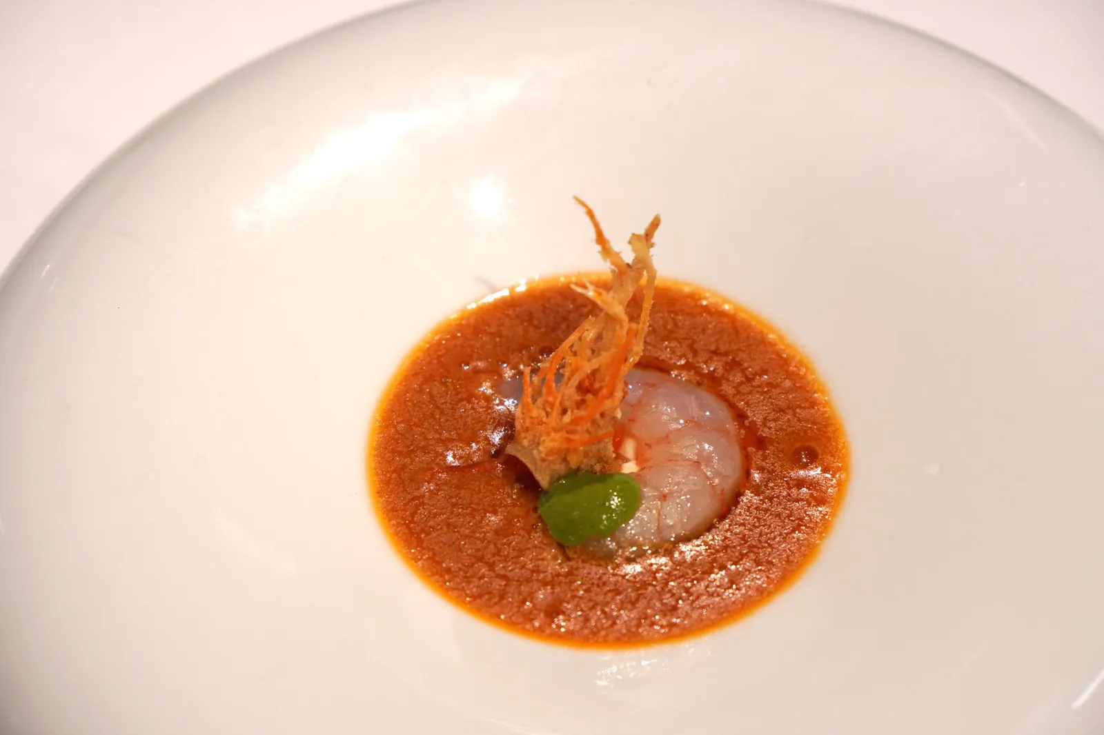 5. Gamba blanca con mojo hervido de sus cabezas y mojo verde de cardamomo. จานนี้เป็นจานที่ดูดีเเละมีศิลปะการปรุงขึ้นมามากกว่าจานก่อนหน้าอย่างเห็นได้ชัด เชฟเลือกใช้กุ้งขาวสดๆ เเละหัวกุ้งทอดกรอบ ทานกับซอสโมโฮพื้นเมือของหมู่เกาะคานารี มีส่วนผสมของพริกไทยดำ กระเทียม และมันจากส่วนหัวกุ้ง นอกจากนี้ยังมีซอสโมโฮอีกอย่างที่แอบซ่อนอยู่ทำจากกระวาน จานนี้พนักงานเน้นย้ำว่าตอนทานต้องทานทุกองค์ประกอบให้ครบในคำเดียว ด้วยความที่เนื้อกุ้งที่สเปนมีรสหวานธรรมชาติมากกว่ากุ้งบ้านเรามากทำให้รสชาติของจานนี้โดดเด่นขึ้นมาจากจานก่อนหน้า หัวกุ้งทอดกรอบทำมห้เกิดมิติทางเนื้อสัมผัสกับเนื้อกุ้งนุ่มๆ ซอสมันกุ้งเเละกระเทียมรสชาติกลมกล่อม มีรสขมเพียงเบาๆมาตัดรสหวานของเนื้อกุ้ง ทั้งยังมีกลิ่นหอมน่ารับประทาน อร่อยสุดๆ (16/20)
