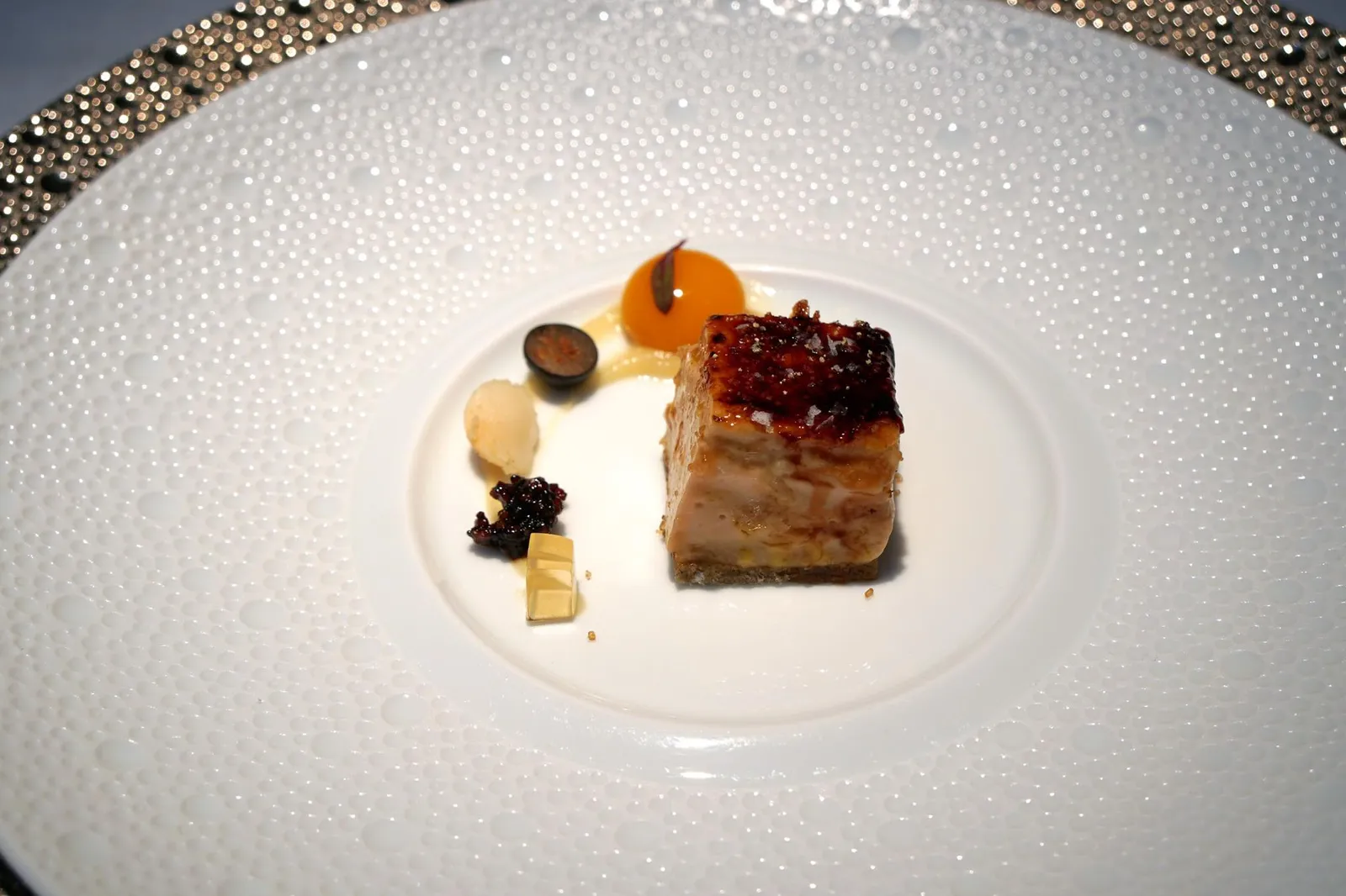 Perfect of FOIE over black sponge cake นี่คืออาหารจานคลาสสิคที่ทำให้ร้าน Cenador de Amós มีชื่อเสียงโด่งดังในหมู่นักชิมชาวยุโรป นั่นก็คือ Perfecto de Foie sobre bizcocho de aceituna negra หรือ Caramelized “Perfect of FOIE” คือ sponge cake ทำจากมะกอกดำ ด้านบนคือสุดยอดตับห่านเนื้อเนียนที่ถูกคาราเมลไลซ์จนเพอร์เฟคตามชื่อ มีเนื้อสัมผัสนุ่ม ละมุนลิ้น สังเกตได้จากเมื่อเขย่าจานเพียงเล็กน้อย ตับก็เด้งไปมาได้ราวกับเจลลี่หรือเครมบรูเล่ทำเอาเราถึงกับทึ่งกับฝีมือเชฟที่สามารถทำเนื้อสัมผัสของตับออกมาได้สุดยอดมากๆ นอกจากรสหวานครีมอันเป็นเอกลักษณ์เเล้ว ยังมีรสขมอ่อนๆบนเลเยอร์ด้านบนที่ถูกคาราเมลไลซ์มาอย่างพอเหมาะพอดี กลิ่นของตับก็หอมสุดๆ ข้างๆกันเป็นเครื่องเคียงให้ทานคู่กันเริ่มจาก Muscat jelly, Tapioca หรือสาคูผสมกับน้ำส้มสายชูจากเมือง Modena, ถั่วแมคคาเดเมีย ผลบลูเบอร์รี่ครึ่งลูก และสุดท้ายคือสเฟียร์มะม่วงรสหวานที่จะเเตกระเบิดออกในปาก นอกจากจะได้ลิ้มรสเนื้อสัมผัสที่เพอร์เฟคของฟัวส์แล้ว เครื่องเคียงต่างๆที่ทานคู่กันยังช่วยทำให้รสชาติที่ได้ทานเเตกต่างกันไปในเเต่ละคำอีกด้วย ถือเป็นการยกระดับเมนูเบสิคทั่วไปให้รสชาติอร่อยเลิศขึ้นไปอีกขั้น เเละเป็นการก้าวข้ามและทิ้งห่างขีดจำกัดเดิมๆของ Foie ไปอย่างขาดลอย (20+/20)