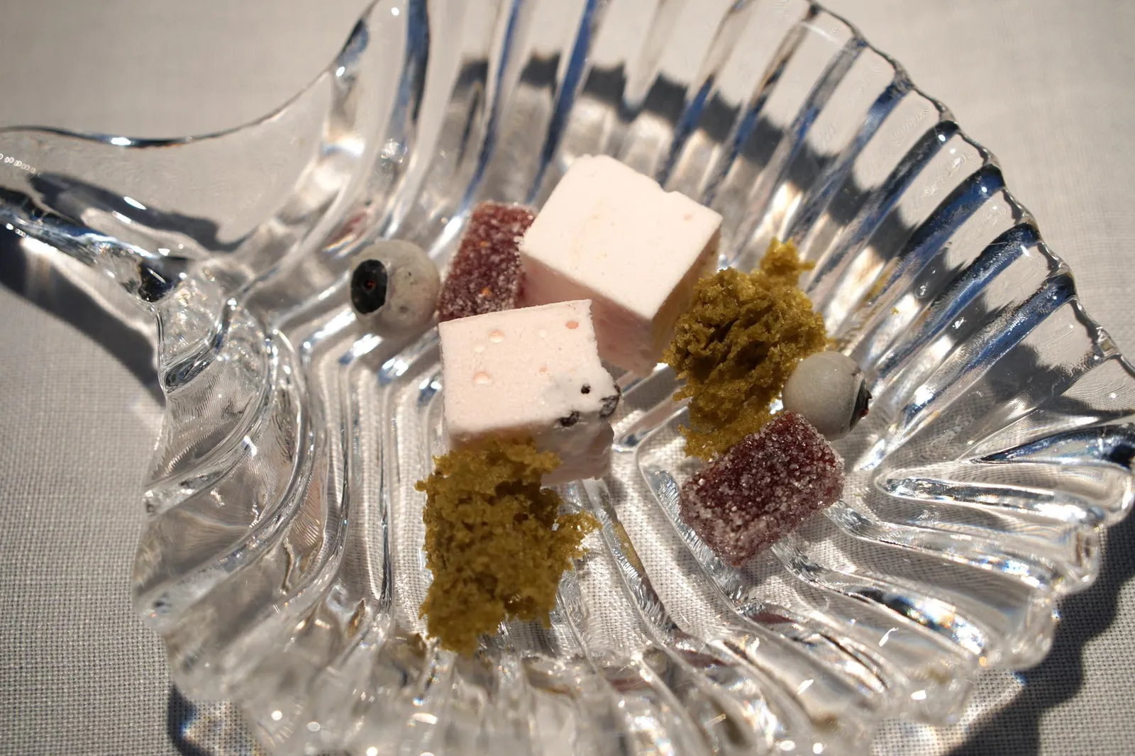 Wild fig jelly, Matcha’s tea Sponge cake, Crunchy blueberries, Watermelon marshmallow เซ็ทเปอตีส์โฟว์เริ่มจากเเถวล่างคือขนมสี่อย่างจัดเสิร์ฟมาในถ้วยเเก้วใสขนาดเล็ก เริ่มจาก Gominola de higo คือเจลลี่สีส้มเข้มเคลือบน้ำตาลทำจากมะเดื่อป่า มีสปองเค้กมัทฉะสีเขียวเรียกว่า Bizcocho de Té Matcha ลูกกลมๆคือ Crujiente de Arándanos เป็นผลบลูเบอร์รี่เคี้ยวกรอบ สีชมพูคือ Marshmallow de sandía ขนมมาร์ชเเมลโล่ที่มีกลิ่นหอมของเเตงโม (20/20)