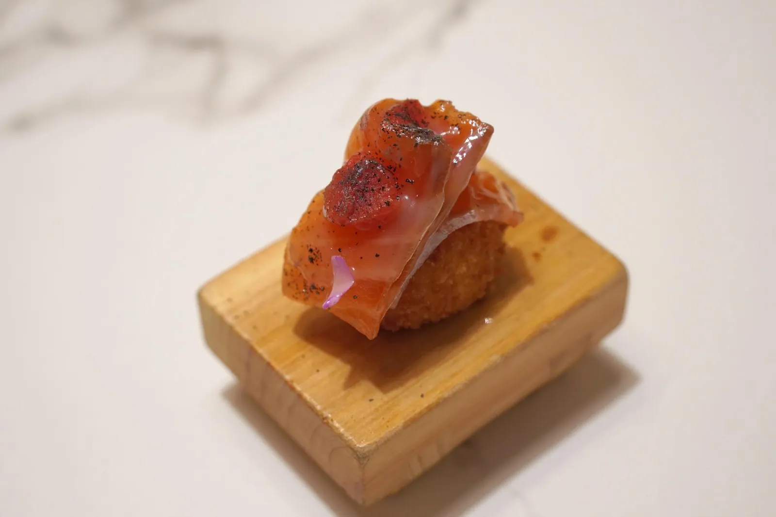 “NIGUIRI-CROQUETTE” MADE OF SHEEP’S MILK AND A “MILEFEUILLES” OF MADURATED SALMON IN JABUGO FAT, TOMATO & SMOKED TEA MARMELADE. โครเก้ทอดกรอบ มีสีเหลืองสวย ภายในบรรจุชีสนมเเกะมีเนื้อสัมผัสกึ่งเหลว มีกลิ่นหอมนวล ด้านบนมีองค์ประกอบสามอย่างถูกจัดเรียงมาเป็นชั้นๆแลดูคล้ายมิลเฟย เริ่มจากปลาเเซลมอนที่ถูกเเช่ในไขมันของหมูดำไอบีเรียจากเมืองจาบูโก้จนอิ่มตัว มะเขือเทศ และแยมที่ทำมาจากใบชารมควัน ไขมันหมูเเทรกเข้าไปในเนื้อของปลาเเซลมอนให้รสเเละกลิ่นที่มีเอกลักษณ์ เเต่ตัดเลี่ยนด้วยความอุมามิของมะเขือเทศ เเละกลิ่นหอมจากผิวด้านบนที่ถูกเเนบด้วยถ่าน (20/20)