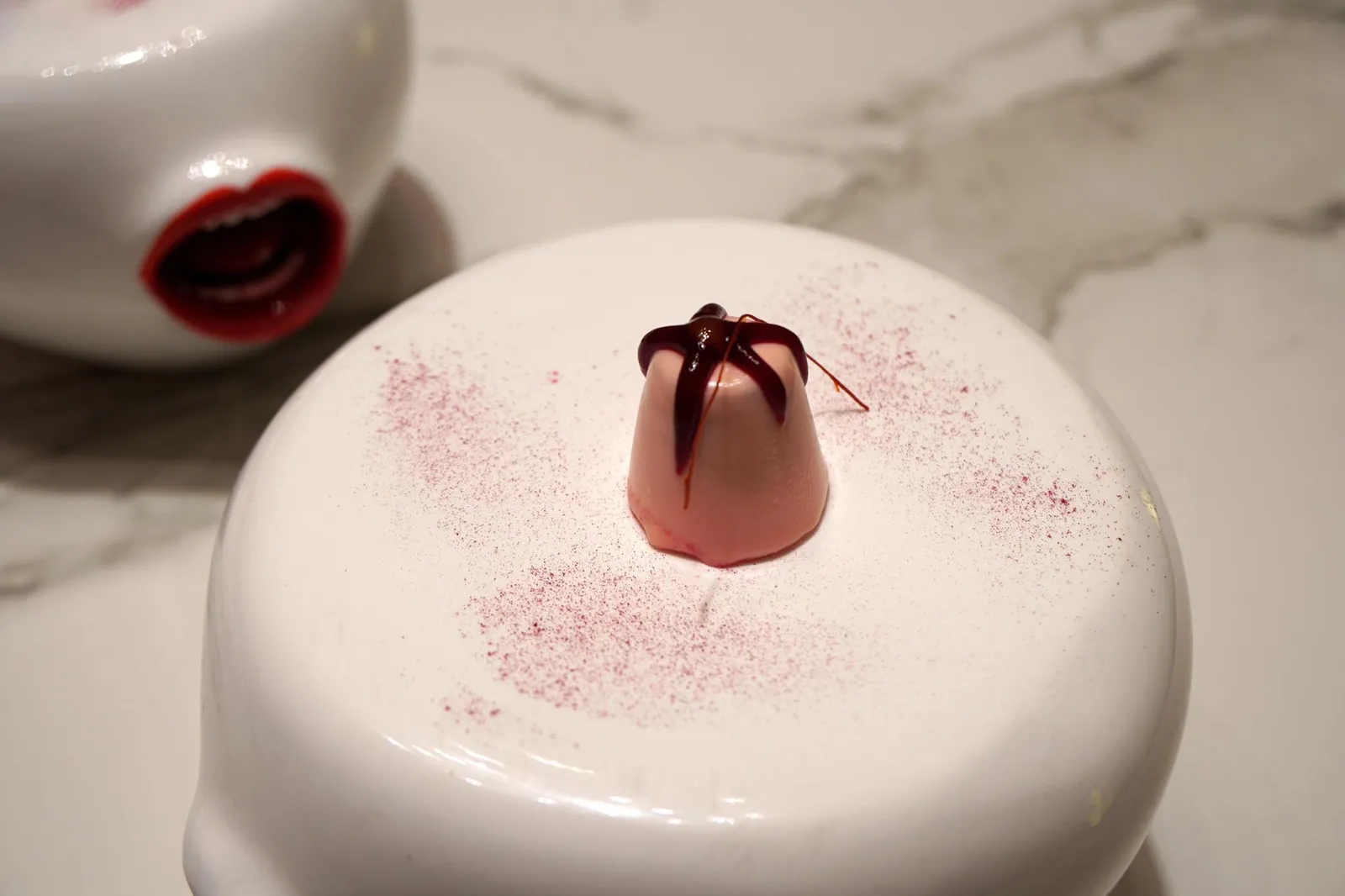 SLIRPING YOUR CHILDHOOD... COTTONCANDY FLAN, BEETROOT, VANILLE AND A TOUCH OF SRIRACHA SAUCE. ขนมฟลานหรือพานาคอตต้ารสสายไหม ทอปด้านบนด้วยบีทรูทเจลลี่สีเเดง และเส้นบางๆทำมาจากซอสศรีราชา เสิร์ฟมาบนจาน!? รูปปากหน้าตาประหลาด วิธีทานที่ถูกต้องคือต้องยกจาน!? รูปปากหน้าตาประหลาดขึ้นมาเพื่อดูดฟลานเข้าปากแบบ one bite อย่าลืมเลียผงบีทรูทรอบๆด้วย ขนมฟลานรสหวาน หอมกลิ่นวานิลลา เป็นหนึ่งในขนมฟลานที่ดีที่สุดเท่าที่ทานมา เจลลี่บีทรูทหนึบๆเพิ่มเนื้อสัมผัส ซอสศรีราชาช่วยเพิ่มกลิ่นให้หอมขึ้นเล็กน้อย มีรสหวานปนเผ็ดเบาๆ (18/20)