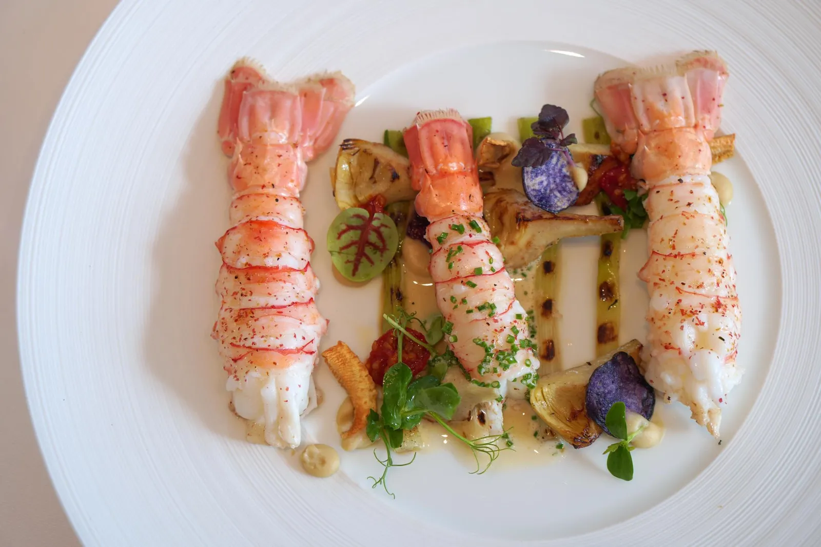 Langoustines »Royales« cooked on Sea salt (69 €) Young Leek จากนั้นจึงนำเสิร์ฟให้กับลูกค้า ภายในจานนอกจากกุ้งขนาดใหญ่ 3 ตัวเเล้วยังมีองค์ประกอบของ Young Leek อาติโชค อาติคย่าง มันฝรั่งม่วง มะเขือเทศ ปิดท้ายด้วยการที่พนักงานราดซอสอาติโชคลงบนตัวชิ้นกลาง และนำซอสวางไว้ข้างๆเพื่อให้ลูกค้าตักราดเองได้ตามใจชอบ (19/20)