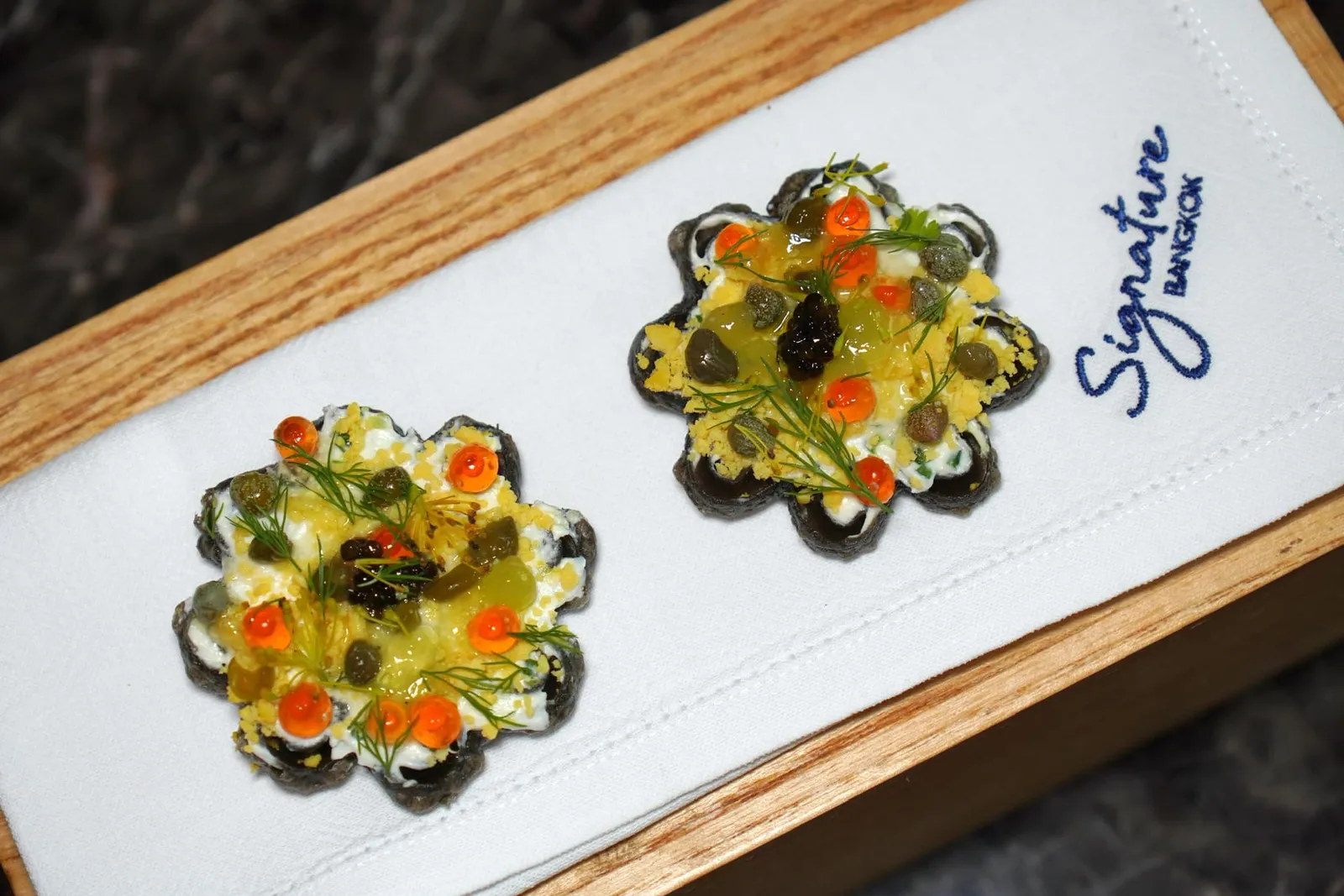 Surprise Canapés Waffle Caviar เป็นเมนูที่เชฟนำเสนอวาฟเฟิลที่มีสีดำจากดีหมึกเคี้ยวกรอบแล้วท็อปด้านบนด้วยคาเวียร์คุณภาพสูง เพิ่มความสดชื่นด้วยไข่มุกที่เตรียมมาจากแตงกวา เพิ่มมิติทางเนื้อสัมผัสด้วยไข่ปลาแซลมอนนั่นเอง (16/20)