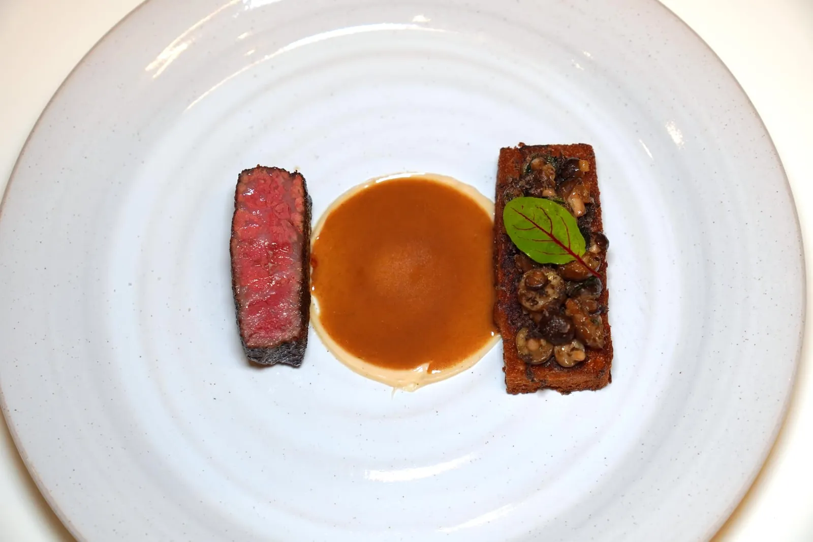Australian Wagyu Striploin MBS8+ with 4 way Mushrooms เมนคอร์สจานเนื้อในวันนี้คือเนื้อวัวออสเตรเลียนวากิวส่วนสันนอกคลุกกับผงเห็ดโมเรล จากนั้นนำไปย่างแล้วเสิร์ฟมาที่ความสุกระดับ Medium Rare อีกฝั่งหนึ่งคือขนมปังบริยอชกรอบนอกนุ่มในท็อปด้วยเห็ดชิเมจิผัด จากนั้นเชฟจะเทราดน้ำซอส Demi Glace ที่ผสมผสานกับน้ำสต๊อปของเห็ดโมเรลเพื่อให้มีความเบาและรับประทานง่ายลงไปตรงกลางจาน