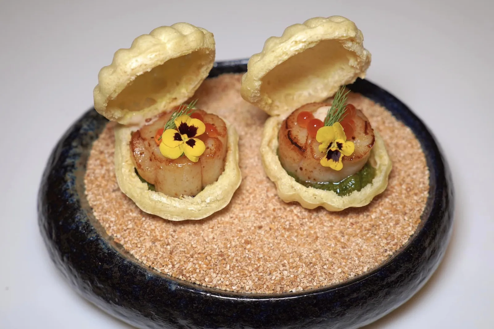 Hokkaido Hotate & Pesto sauce with Jasmine rice cracker แครกเกอร์กรอบที่เชฟเตรียมขึ้นมาจากข้าวหอมมะลิไทยประกอบรูปร่างเป็นฝาหอย ตรงกลางคือหอยเชลล์โฮตาเตะขนาดมาตรฐานจี่บนกระทะจนนุ่มและหวาน ด้านล่างคือซอส Pesto และเฟนเนลให้กลิ่นและอโรมาเฉพาะตัว