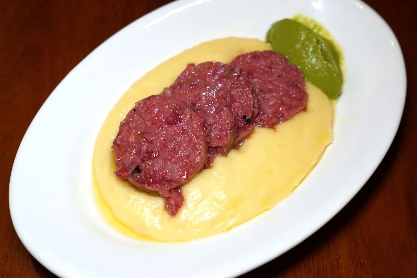 Il Cotechino Di Modena Con Crema Di Pate (290++) Slow cooked traditional Emilia succulent pork sausage, creamed potatoes. “โกเตชชิโน่ ดิ โมดิน่า” คือไส้กรอกพื้นเมืองที่มีต้นกำเนิดมาจากเมือง Modena ว่ากันว่าในช่วงสมัยปี ค.ศ. 1522 โดยชาวเมืองที่กำลังหิวโหยจากการถูกล้อมเมืองในภาวะสงครามต้องการหาหนทางที่จะเก็บรักษาเนื้อเอาไว้ให้นานที่สุดและคิดค้นสูตรการทำไส้กรอกชนิดนี้ขึ้นมาโดยมีองค์ประกอบหลักคือเนื้อหมูและไขมันหมู ทางร้านนำมาผ่านกระบวน Slow cooked ช้า ๆ จนสุก ทานแล้วจะสัมผัสได้ถึงความนุ่ม ละมุน และความฉ่ำของเนื้อหมู มีรสชาติออกเค็มนิด ๆ แนะนำให้ทานสลับกับครีมมันฝรั่งที่รองอยู่ด้านล่างและซอสพาสลีย์ข้าง ๆ กัน (13/20)