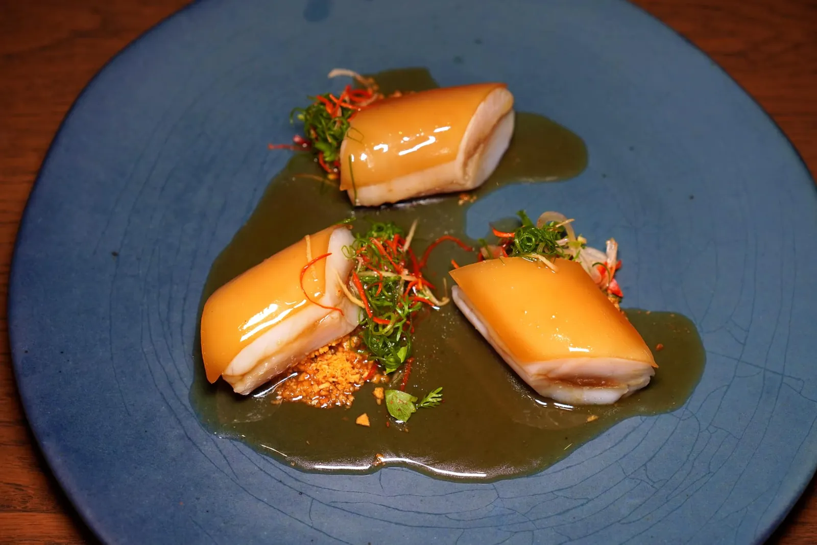 “Baked Fish, In House Soy Sauce, ปลาบู่อบซีอิ๊ว” สำหรับคอร์สปลาเชฟเลือกใช้ปลาบู่ที่เตรียมมาด้วยวิธี Ikejime ก่อนจะนำไป Dry-Aged นานถึง 3 วัน ด้านบนคือเจลนุ่ม ๆ ที่เตรียมขึ้นมาจากน้ำซีอิ๊ว เลเยอร์ตรงกลางของชิ้นปลาเป็นองค์ประกอบของหัวหอมแดงช่วยลดทอนกลิ่นดินของปลาบู่ได้อย่างเหมาะเจาะ เชฟจับคู่มากับสมุนไพรและกระเทียมเจียวข้าง ๆ กัน จากนั้นเชฟจะมาเทราดซอสซีอิ๊วสูตรพิเศษลงไปรอบ ๆ จาน (14/20)