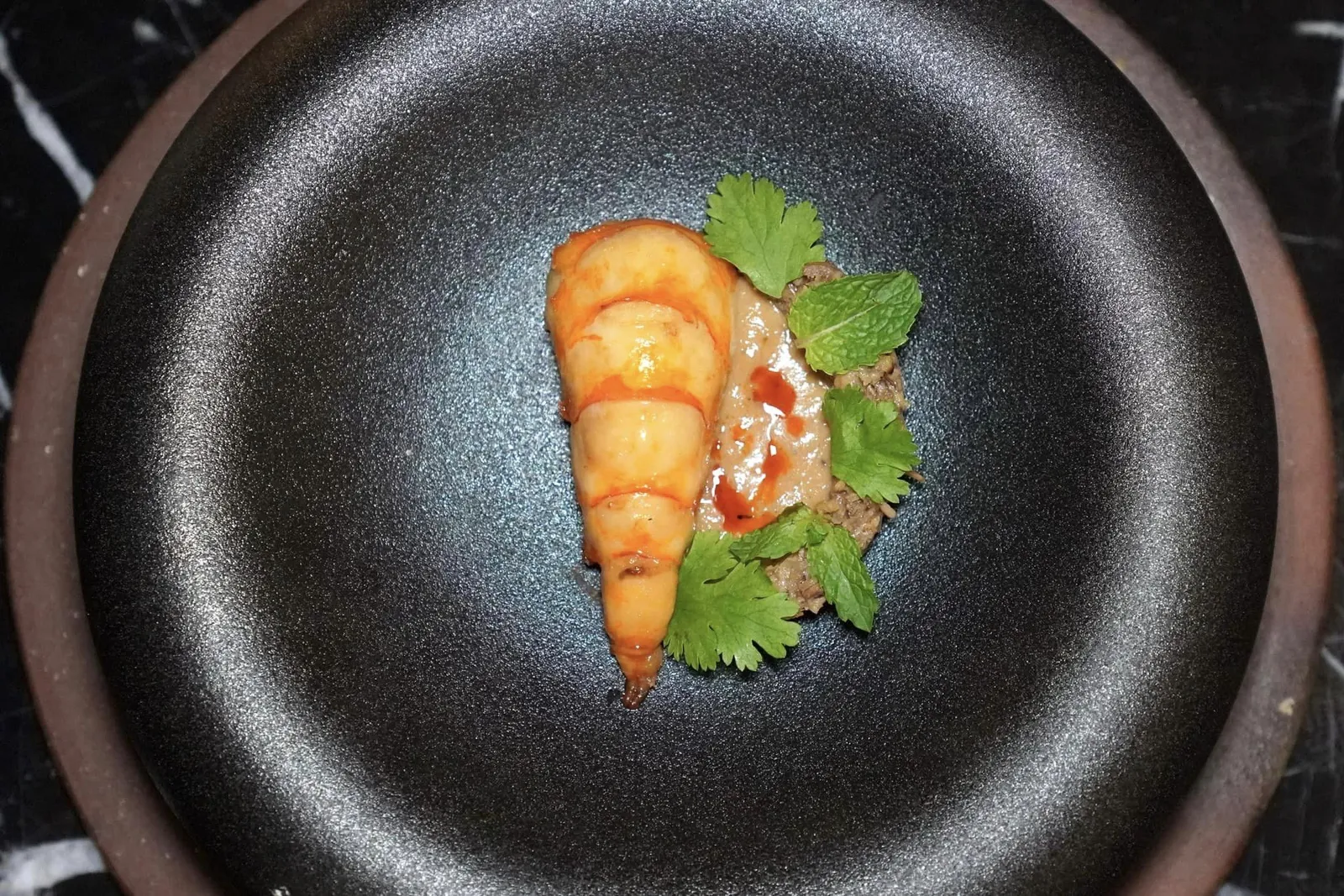 Nam Prik Nam Ya Ayutthaya scape - Fresh River Prawns | Banana Blossom | Sesame Paste | Bitter orange กุ้งย่างน้ำปลา น้ำยาน้ำพริก หัวปลี ส้มซ่า เมนูนี้เชฟเทพตั้งใจสื่อถึงภูมิทัศน์ของจังหวัดอยุธยาที่มีแม่น้ำป่าสักไหลผ่านและมีความอุดมสมบูรณ์ไปด้วยกุ้งแม่น้ำและต้นกล้วยมากมาย เชฟนำกุ้งแม่น้ำไปหมักกับน้ำปลาจนเข้าเนื้อแล้วย่างให้เกือบสุกจนได้เนื้อสัมผัสที่กรอบสู้ฟัน ข้างกันคือซอสน้ำยาน้ำพริกที่เตรียมขึ้นมาจากกะทิ พริกแห้ง และถั่ว ก่อนจะเสิร์ฟมาคู่กันกับยำหัวปลีที่มีเนื้อสัมผัสตัดกันกับตัวกุ้งโดยมีความฉุนของผักชีมาช่วยเบรคความมันของน้ำยาไม่ให้โดดจนเกินไป (15/20)