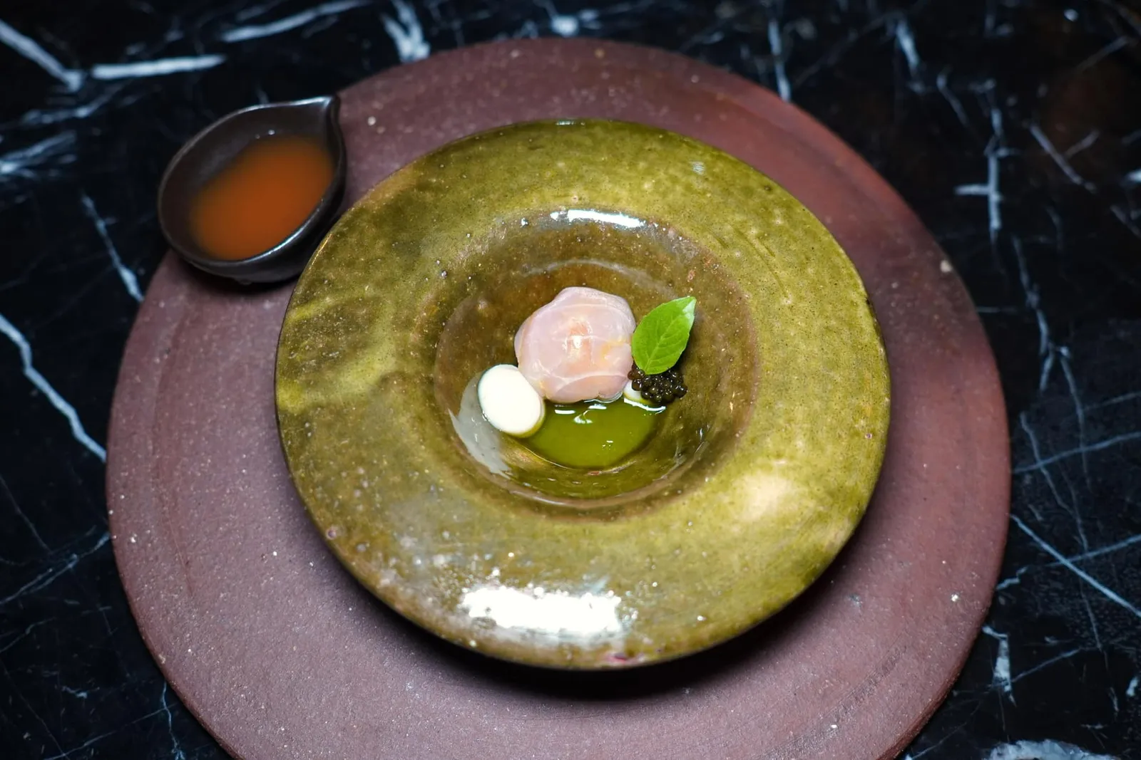 Pla Dib Cured Curry Salt | Tomato Consomme Okra | Basil oil ปลาดิบบ่มพริกแกง แกงส้มมะเขือเทศใส่กระเจี๊ยบสด น้ำมันโหระพา ”ปลาดิบ“ ได้จากการนำปลากระพงไปบ่มกับพริกแกงฉู่ฉี่จนเข้าเนื้อ จากนั้นยัดไส้ด้วยพริกสามสีเพื่อปรุงรส ข้างกันคือซาวครีมที่เตรียมมาจากข้าวหมากไทยช่วยเพิ่มมิติทางเปรี้ยวแบะครีมมี่ ยังมีไทยคาเวียร์จากอำเภอหัวหินเติมแต่งรสเค็มได้อย่างพอเหมาะ ด้านล่างรองด้วยน้ำมันใบโหระพาสร้างกลิ่นฉุนมาตัดกันกับอโรมาของพริกแกง ไฮไลท์ของจานคือคอนซอมเม่ใสที่เตรียมมาจากมะเขือเทศและกระเจี๊ยบให้ความสดชื่นและอุมามิ ก่อนชิมหลายคนอาจนึกรสชาติไม่ออกแต่หลังจากได้ลองชิมพบว่าปลาดิบและพริกแกงสามารถผสมผสานเข้ากันกับองค์ประกอบอื่น ๆ ได้อย่างน่าทึ่งจนรับรู้ได้เลยว่านี่คือการรังสรรค์ใหม่ที่ผ่านกระบวนการคิดและทดลองมาอย่างลงตัว (15/20)