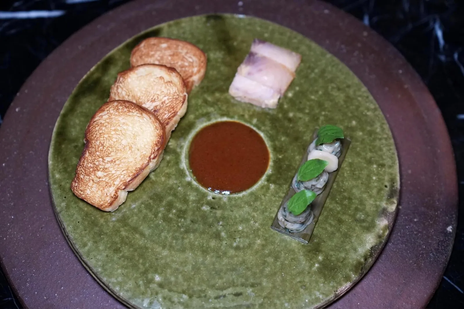 Ngao-Ngod Bread & Bisque - Baked Steamed Pang-Pao | Smoked Pangasius | Portuguese-Influenced Bisque แกงเหงาหงอด เปาปังบริยอช เนยปลาจ่อม ปลาสังกวาสย่างรมควัน บิสก์ปลาแห้งไวน์กระชาย ใบโหระพา ”แกงเหงาหงอด“ เป็นแกงโบราณที่สูญหายไปนาน เชฟเสิร์ฟมาในสไตล์ของฝรั่งโดยใช้ขนมปังบริยอชกรอบนอกนุ่มในจับคู่มากับเนื้อปลาสังกวาสย่างและรมควันต่อจนได้เนื้อสัมผัสที่เฟิร์มแต่ไร้ซึ่งความกระด้าง ข้างกันคือเนยปลาจ่อมหรือปลาร้าที่บาลานซ์กลิ่นมาดีมาก ๆ คล้ายกันกับเนยแองโชวี่ของฝรั่งรับประทานง่ายโดยไม่มีกลิ่นติดในปาก ตรงกลางคือซอสแกงเหงาหงอดที่ได้รับแรงบันดาลใจจากชาวโปรตุเกสเสิร์ฟมาในสไตล์ของบิสก์ที่ไม่เข้มข้นหรือใสจนเกินไป ตัวแกงในสมัยนั้นมีองค์ประกอบเป็นใบโหระพาด้วยเชฟจึงแปะใบโหระพามาบนชิ้นเนย วิธีรับประทานให้หยิบทุกองค์ประกอบวางลงบนเปาปังคล้ายกับกันโอเพ่นแซนวิชนั่นเอง (15/20)